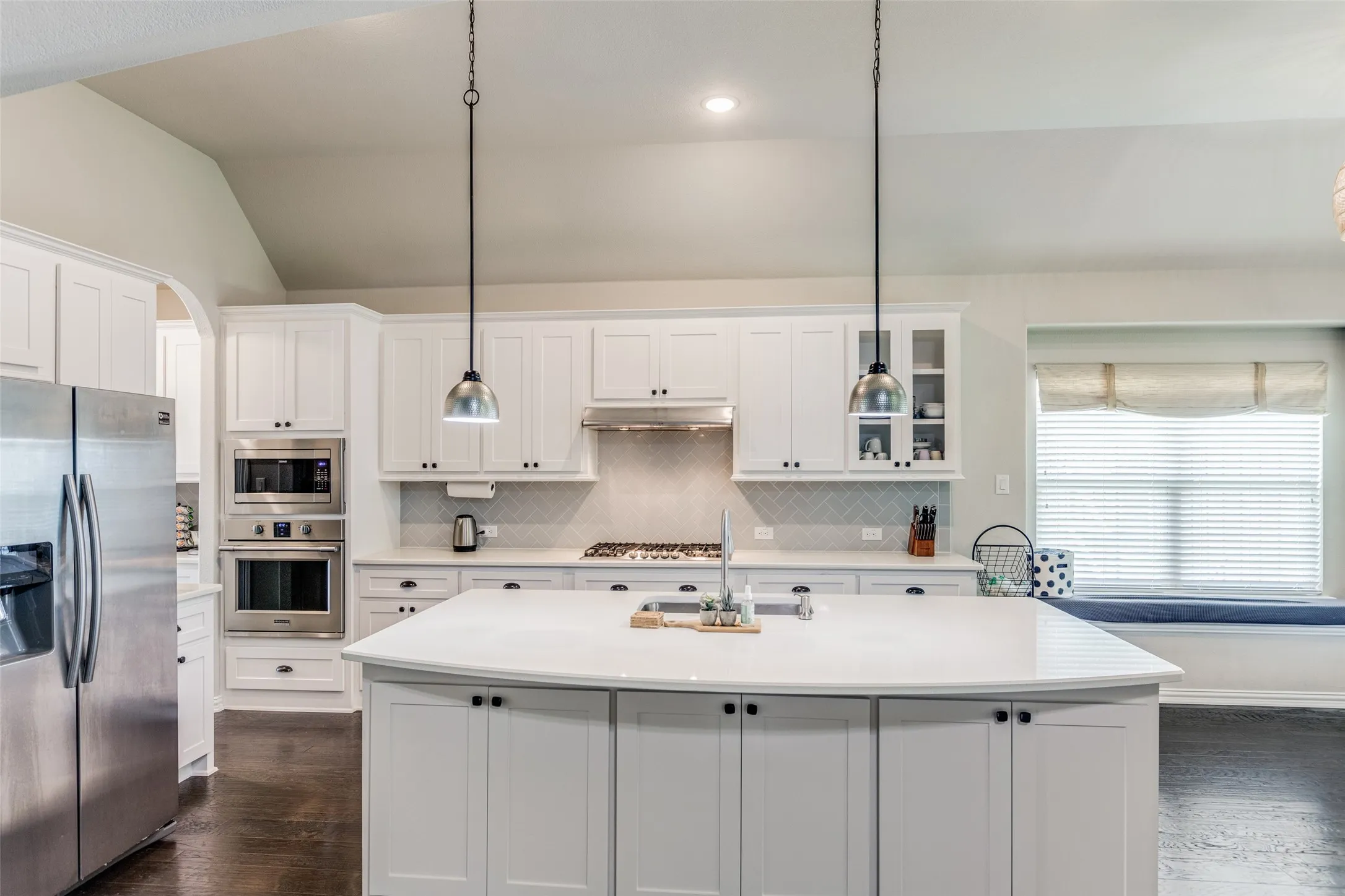White shaker cabinetry, stainless steel appliances, central island with solid surface countertop, white subway tile backsplash, and vaulted ceiling