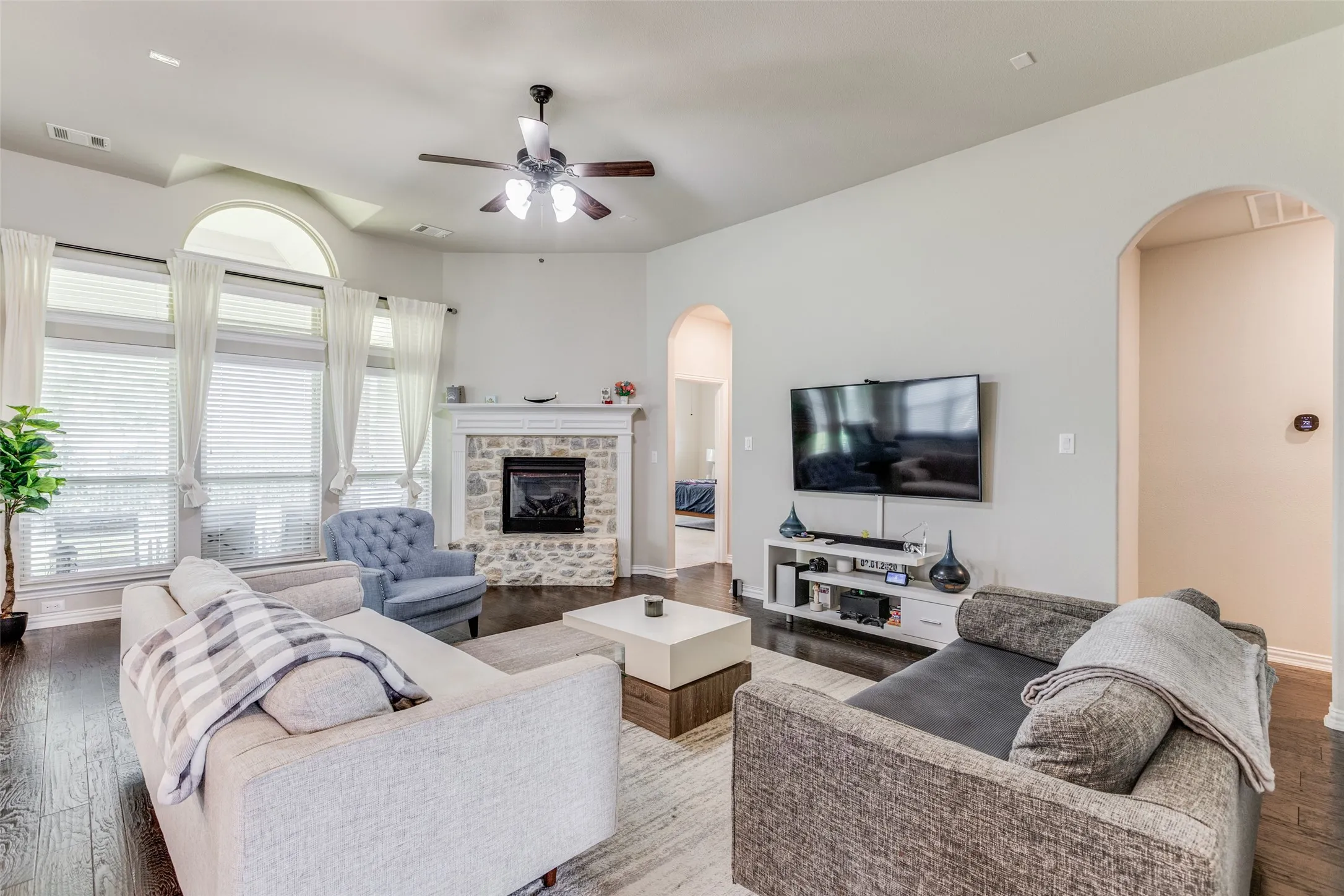Living area with wood-finish flooring, a stone-surround fireplace with a mantel, and an arched window