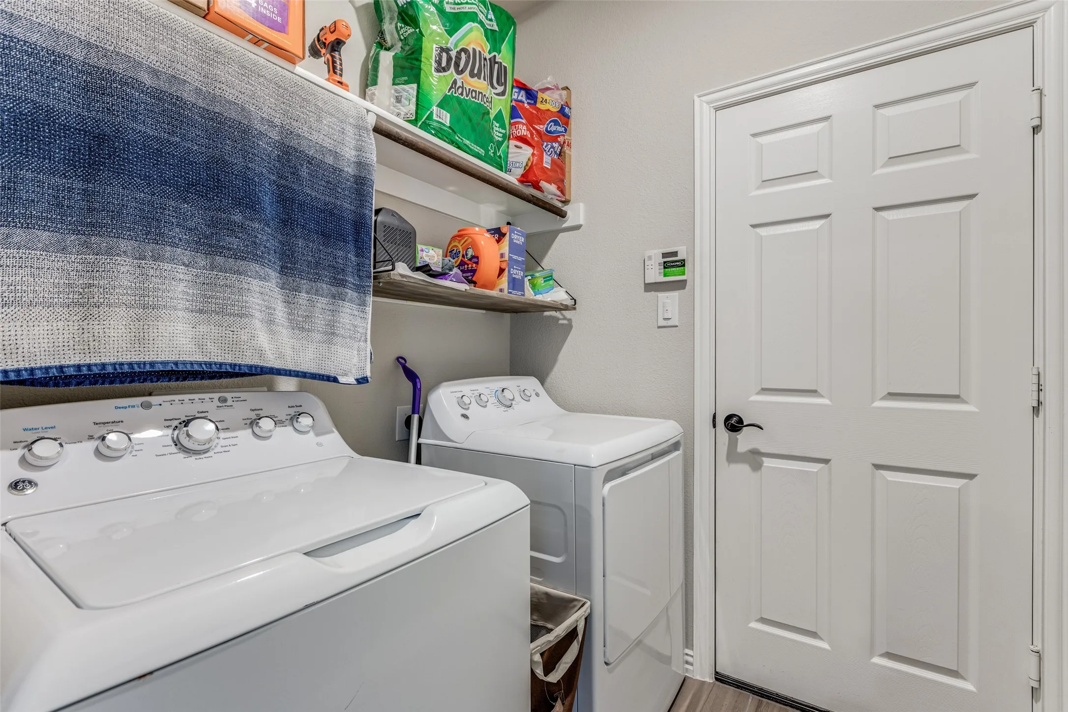 Laundry area featuring white appliances, floating wood-finish shelving, and a paneled door with dark hardware
