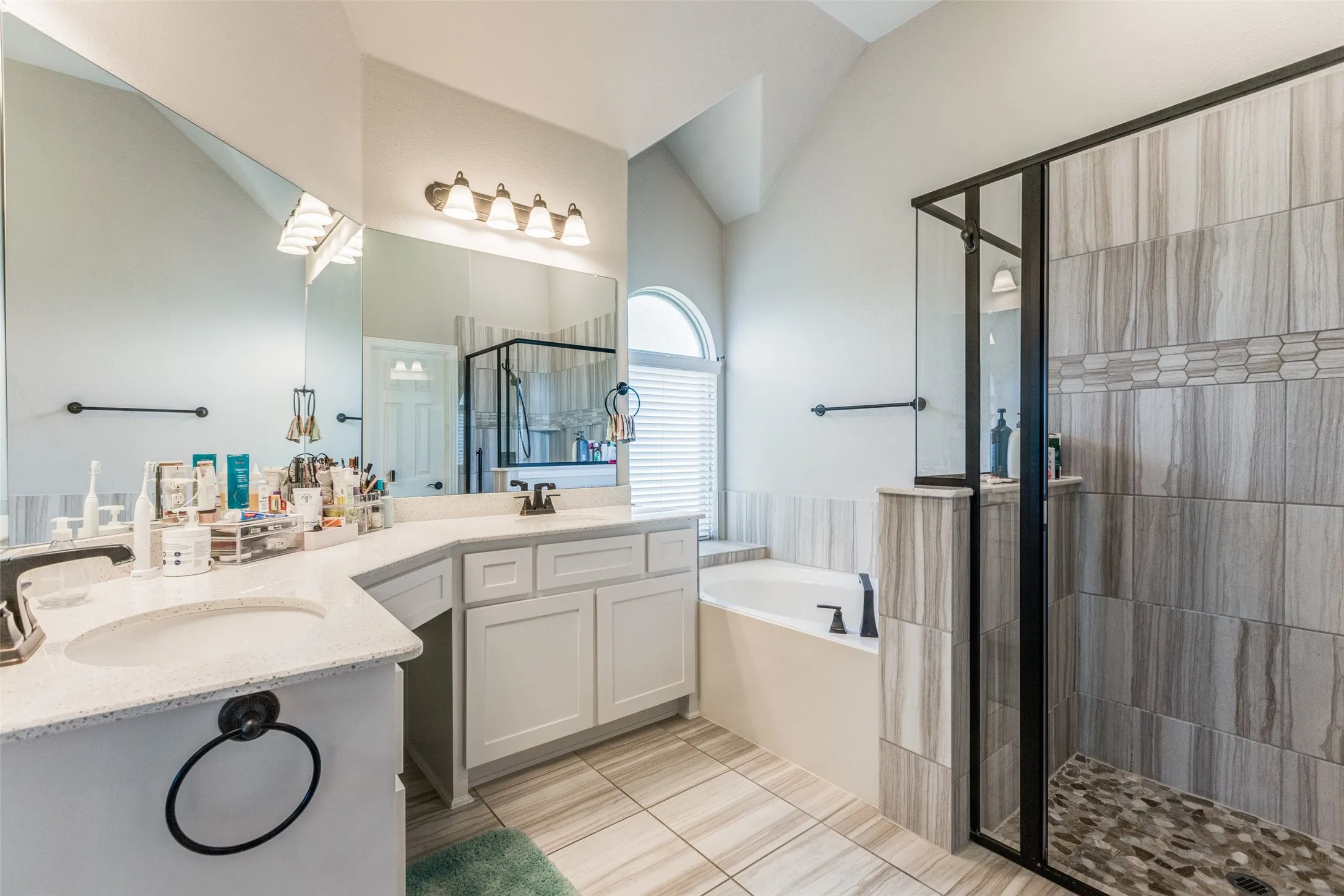 White shaker cabinetry with stone countertops, a built-in soaking tub, and a separate glass-enclosed shower featuring stone tile
