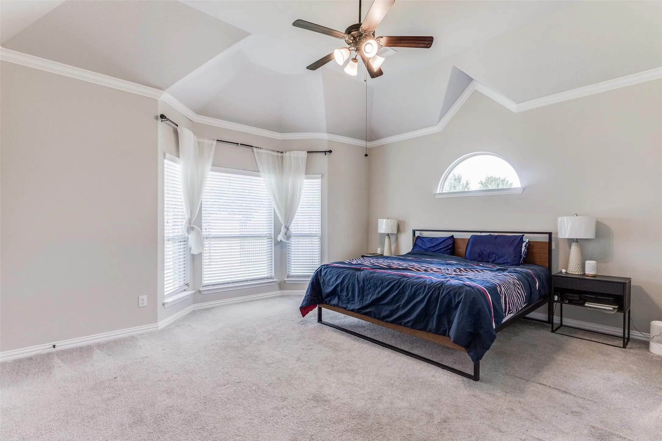 Tray ceiling with crown molding, ceiling fan with integrated lighting, bay window, arched window, and neutral wall color