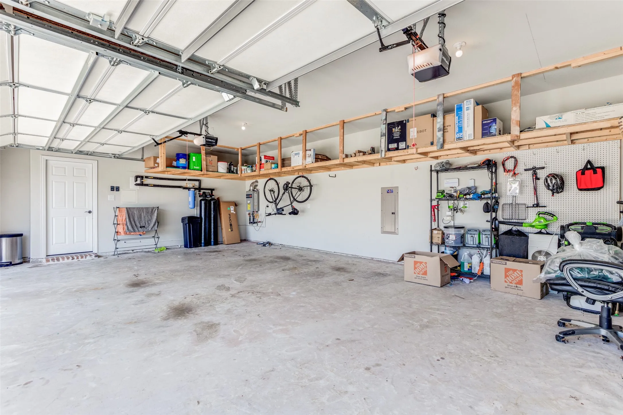 Spacious garage featuring high ceilings, overhead garage door system, built-in shelving, and direct door access