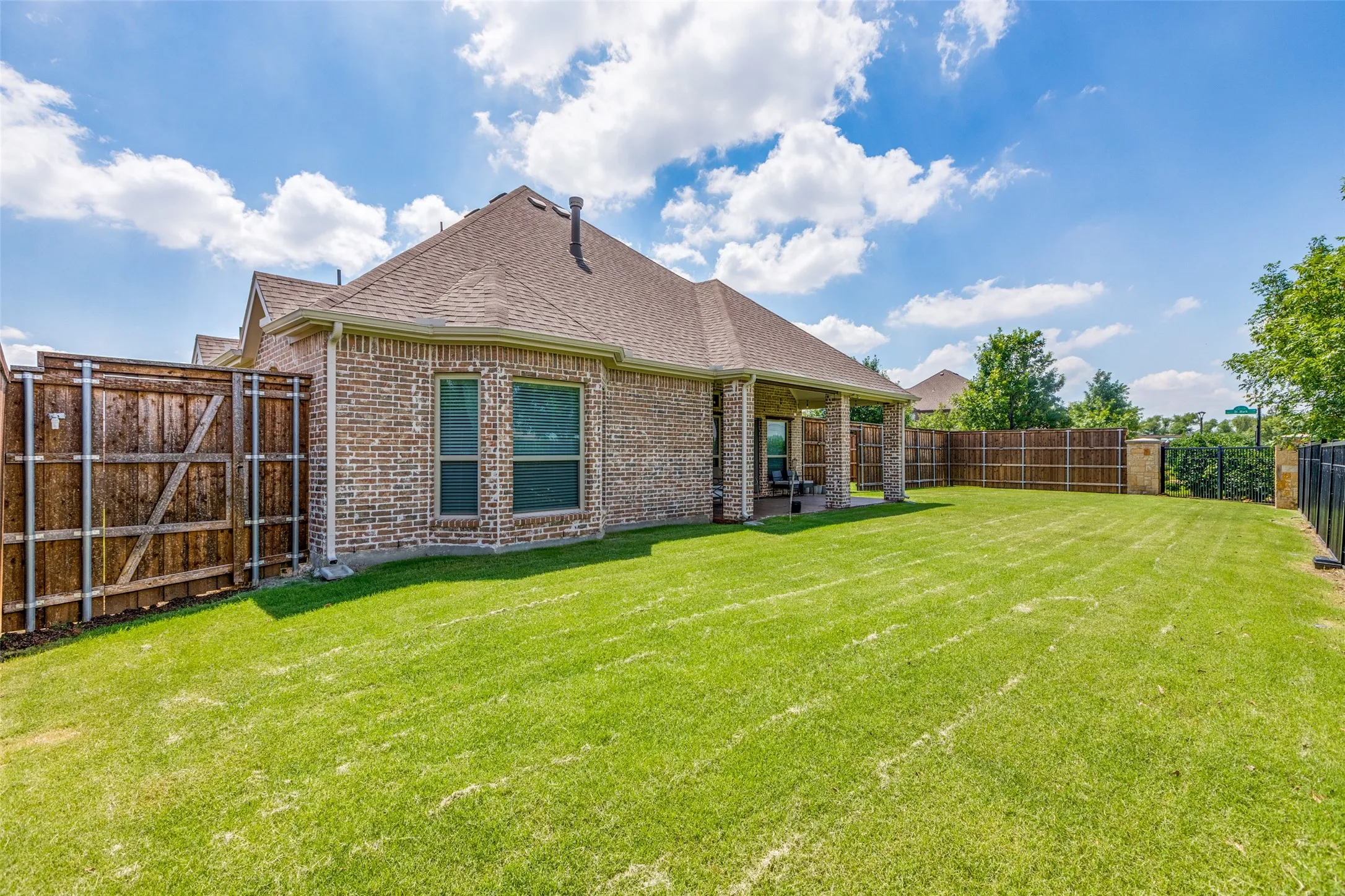 Brick exterior with multiple windows, covered patio with structural columns, expansive lawn, and wooden privacy fencing