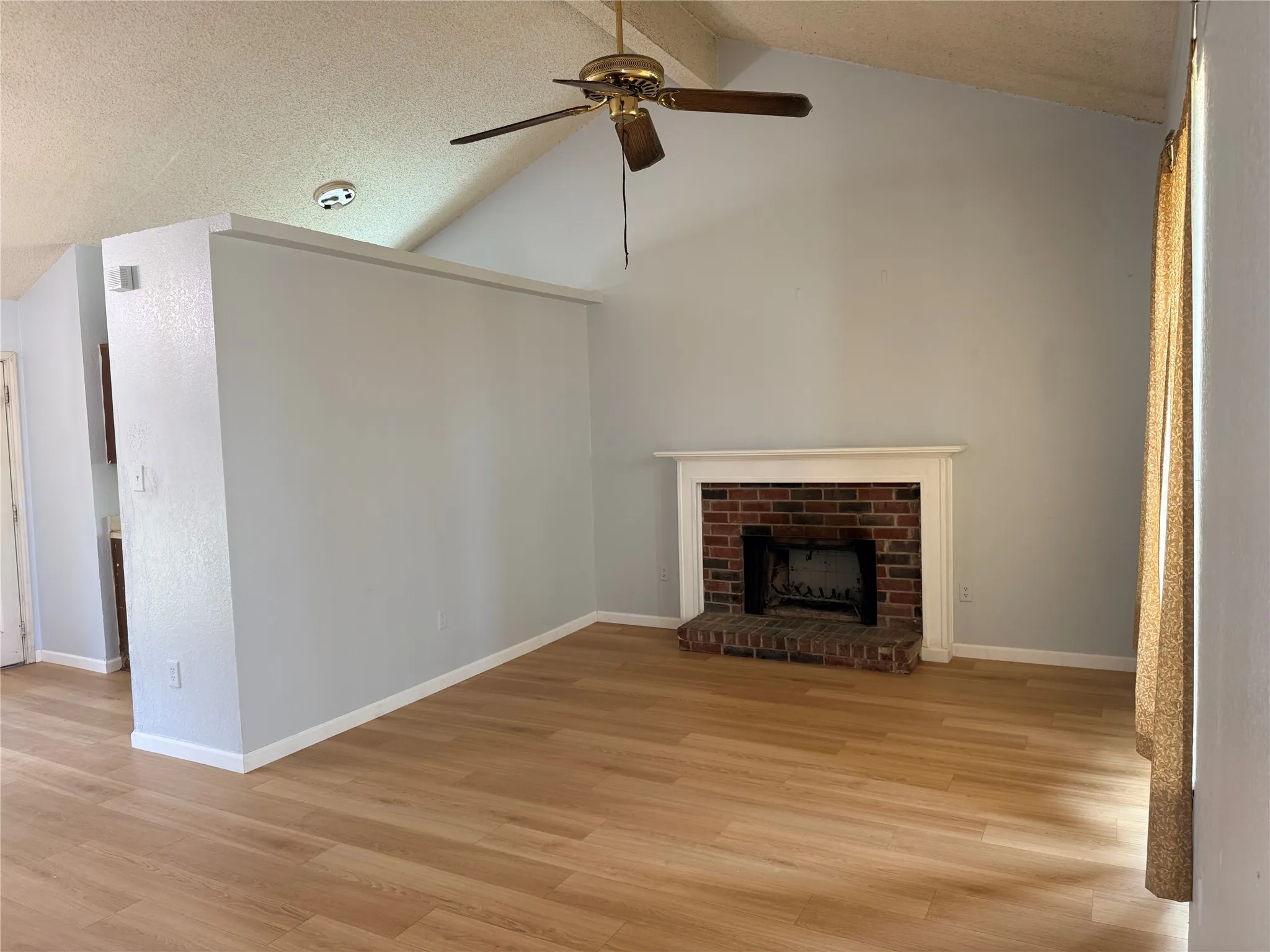 Vaulted ceilings with a ceiling fan, brick fireplace with a white mantel, and wood-finish flooring