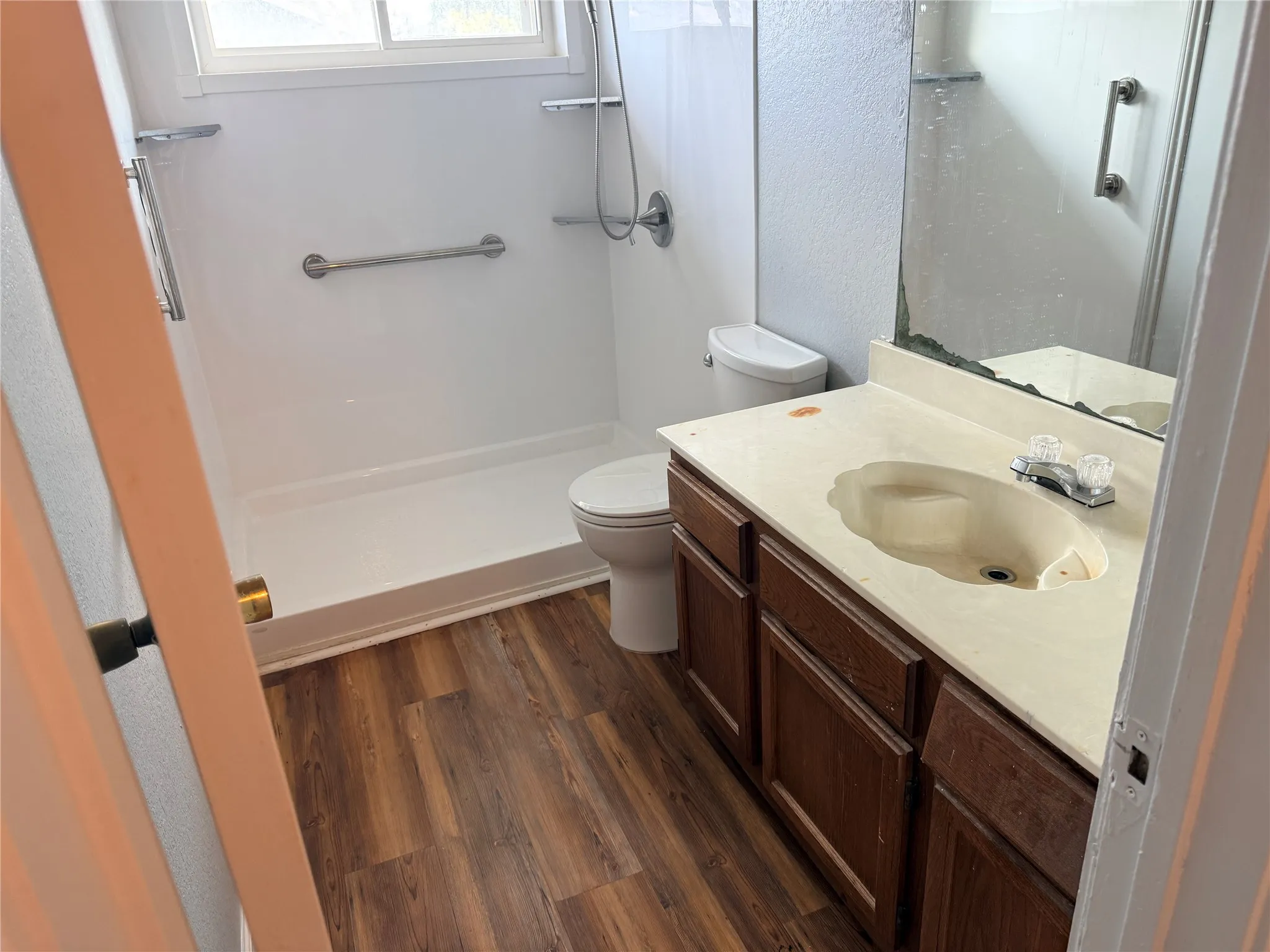 Bathroom featuring wood-finish flooring, a vanity with a light-colored countertop and integrated sink, and a shower with a grab bar