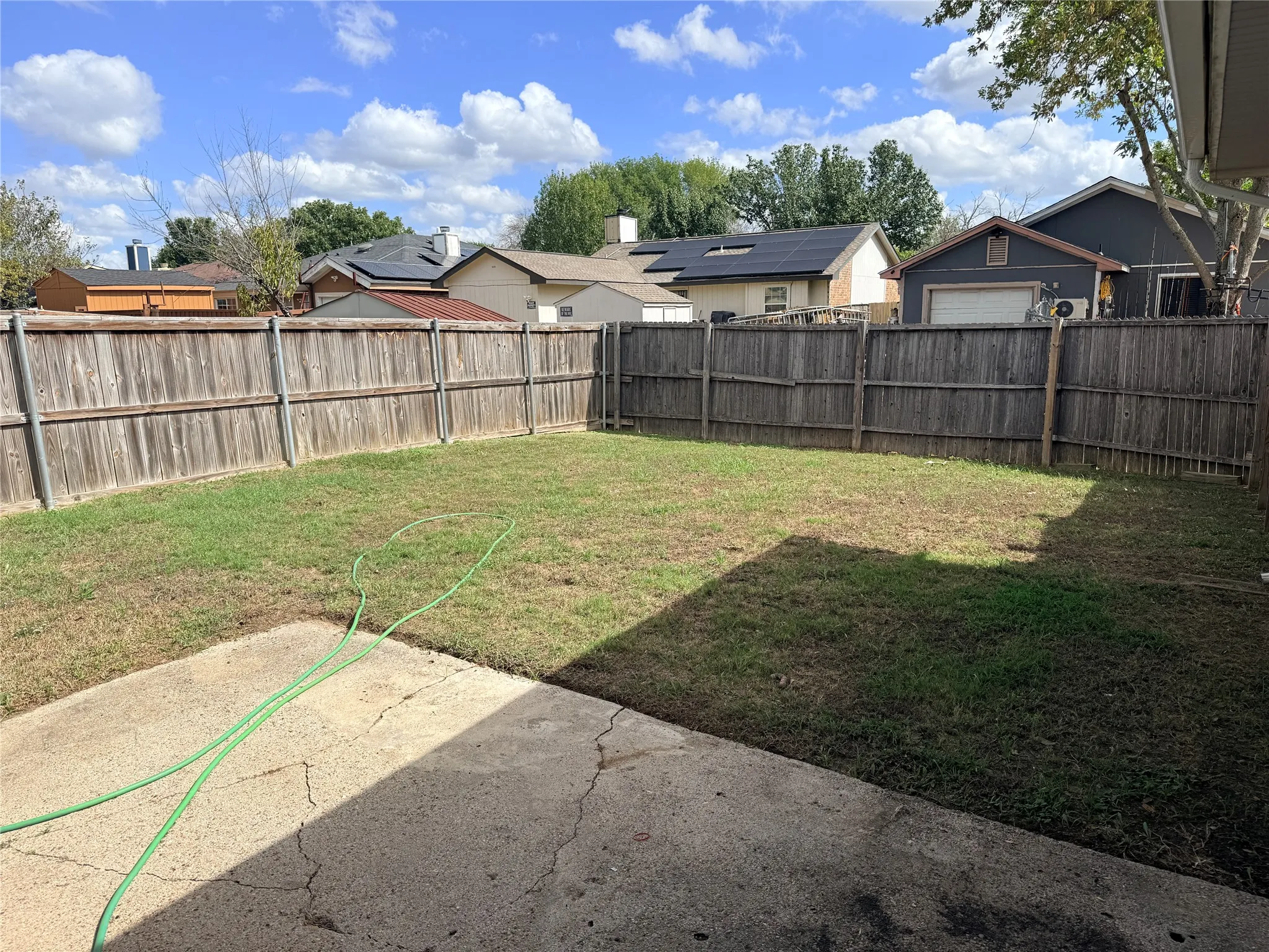 Expansive backyard featuring a wood privacy fence, concrete patio, and a grass lawn