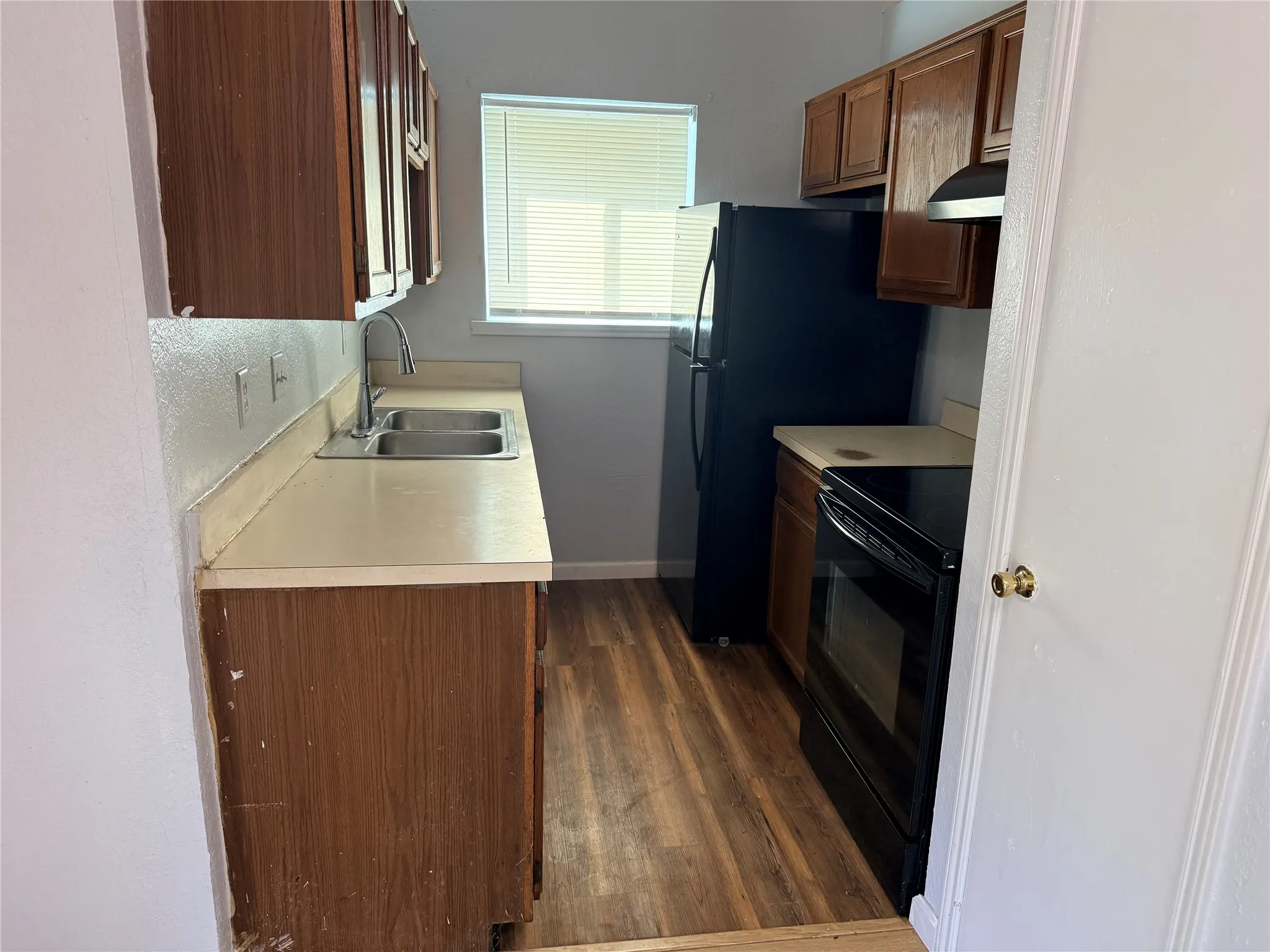 Wood-finish flooring, dual basin stainless steel sink, black range, and refrigerator