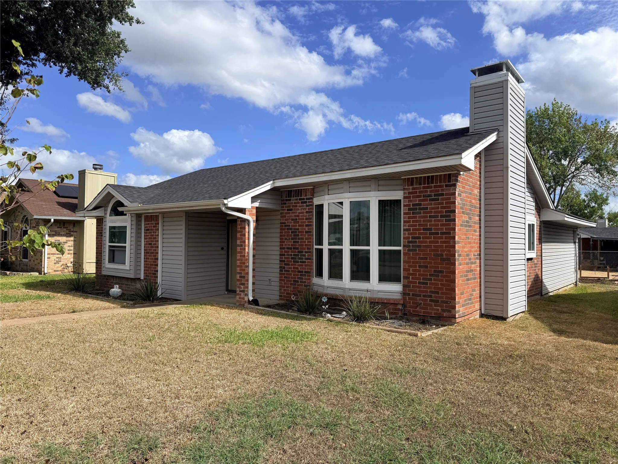 Brick and siding exterior with a dark shingle roof, featuring a prominent bay window and a stone-clad chimney