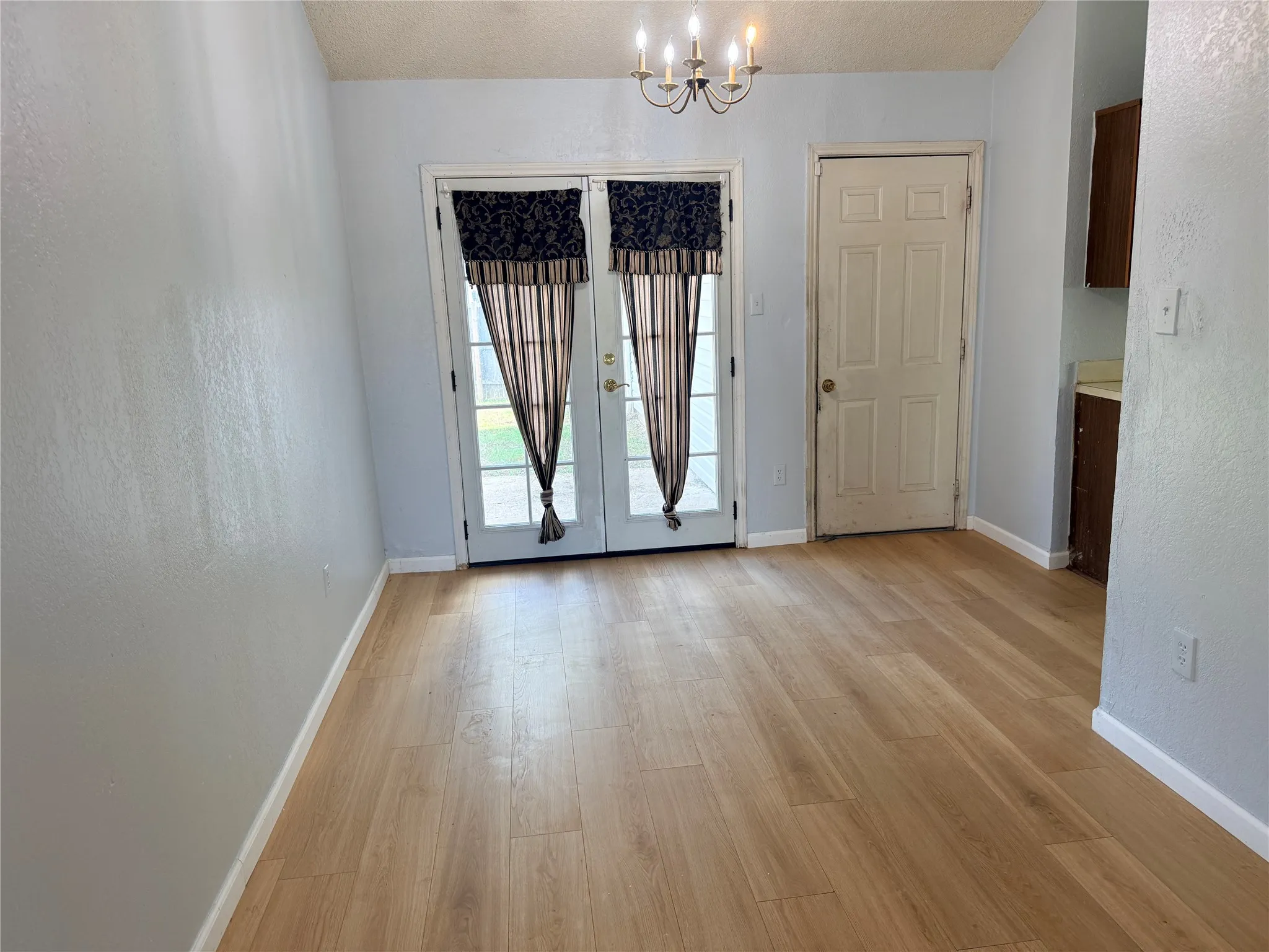 Light wood-finish flooring with a multi-paneled double door and a chandelier light fixture