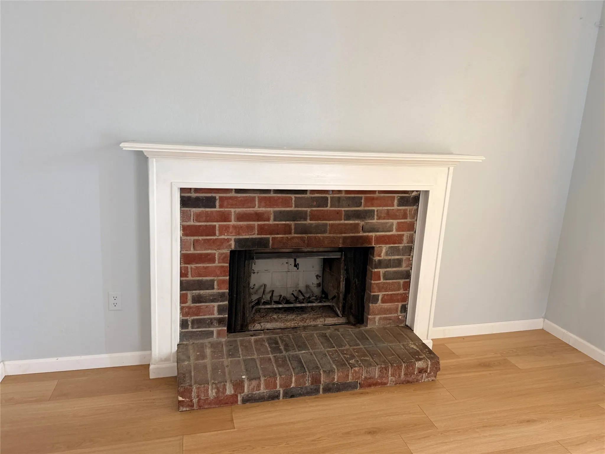 Brick fireplace with a white mantel and hearth, complemented by wood-finish flooring