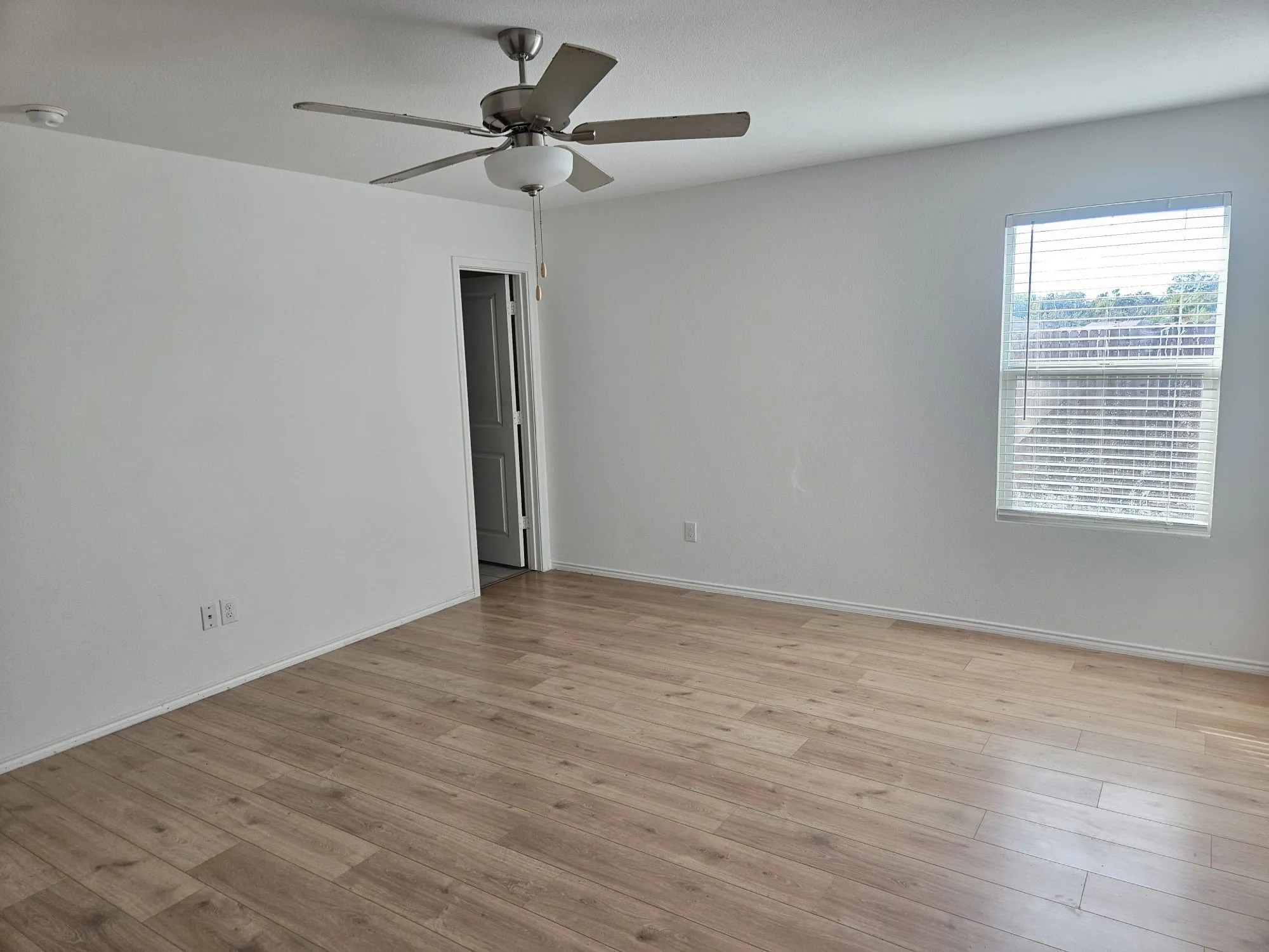 Wood-finish flooring with neutral wall paint, overhead ceiling fan with lighting, and a window with blinds