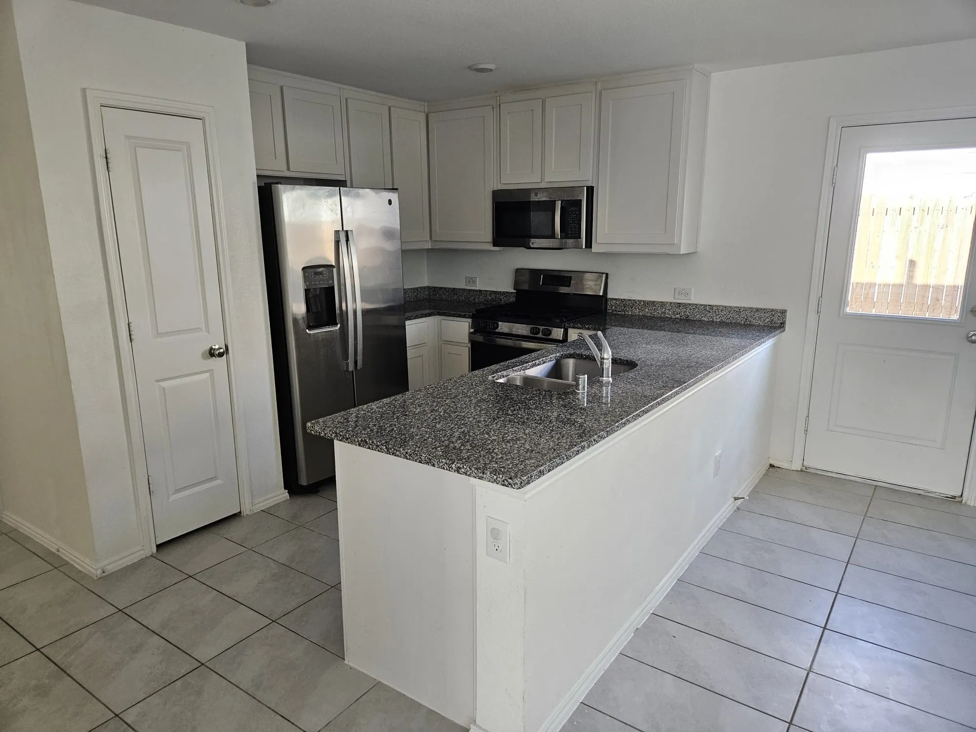 White upper and lower cabinetry, stainless steel appliances, granite countertops, tile flooring, and a glass-paned exterior door