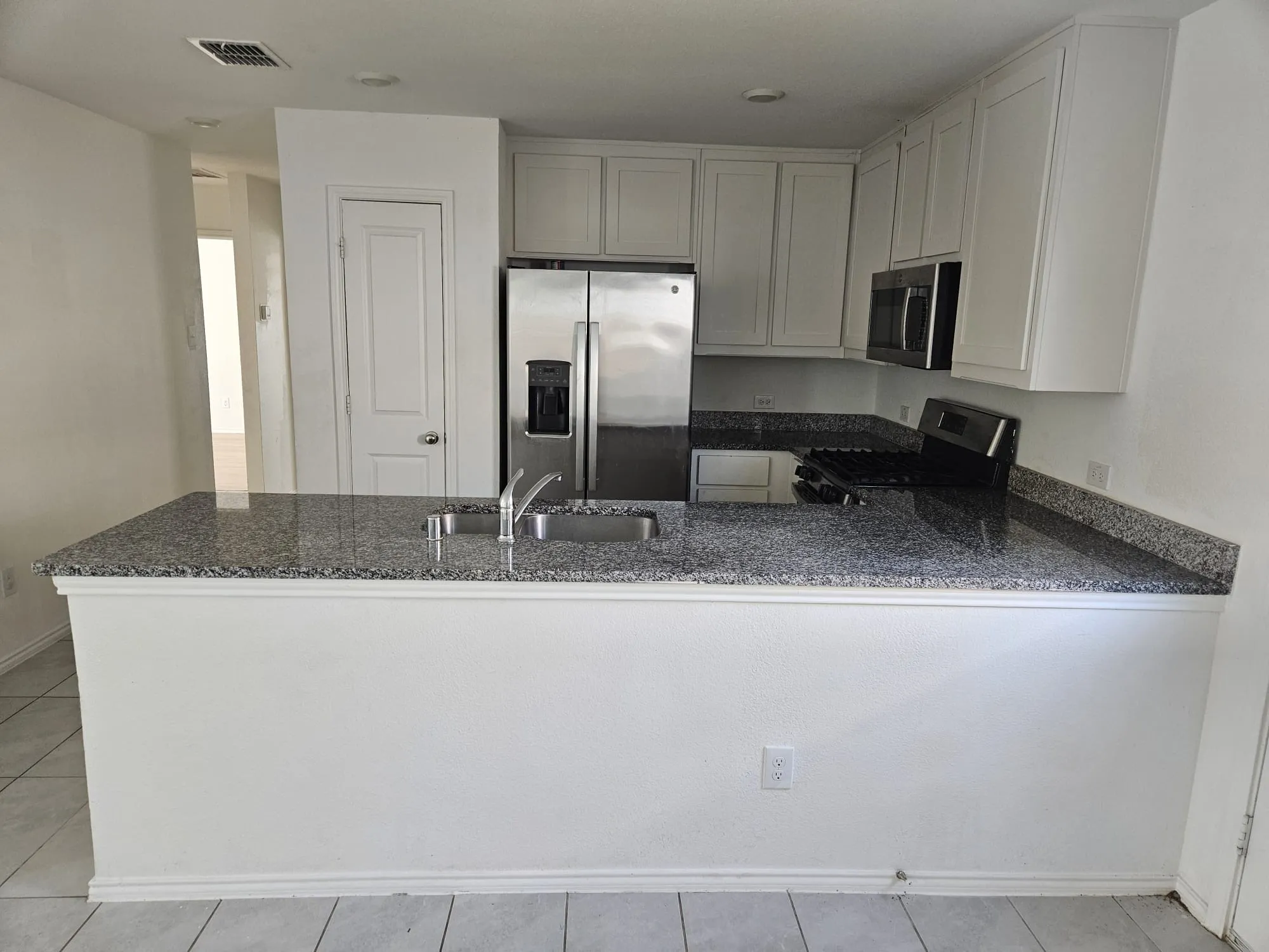 Granite-style countertops, stainless steel refrigerator, white cabinetry, integrated sink, and tile flooring