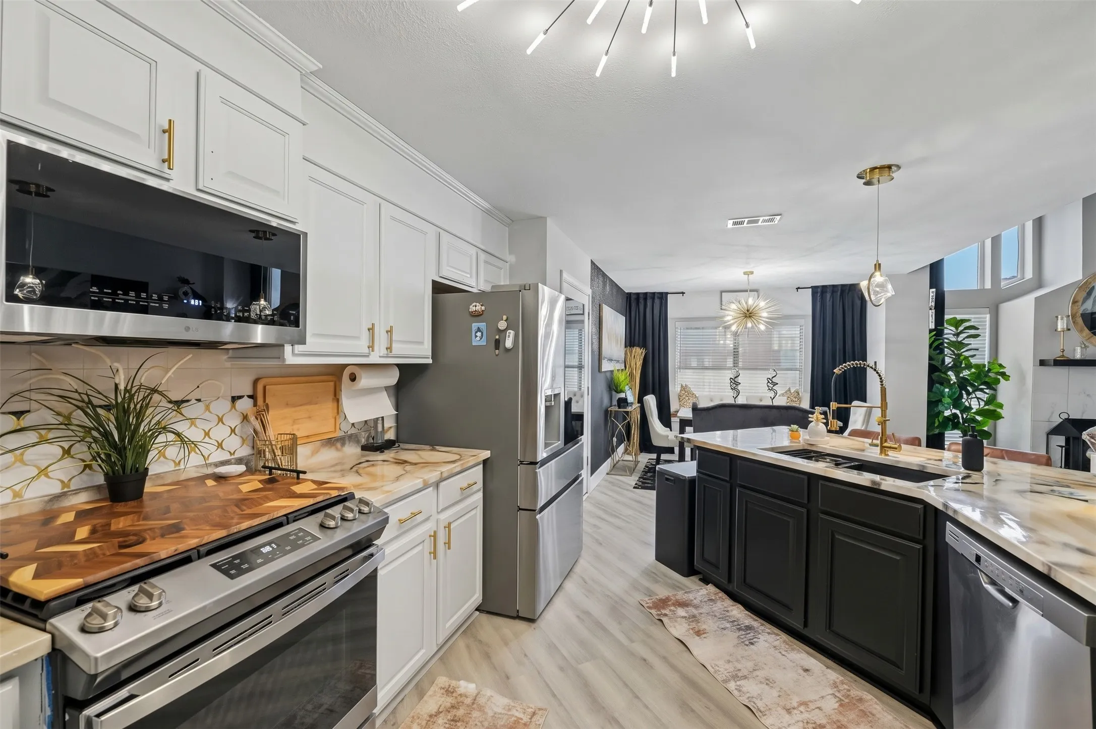 Kitchen featuring light wood-finish flooring, white upper cabinetry with gold-tone hardware, a black kitchen island with gold-tone faucet, stainless steel appliances, and high ceilings with recessed lighting
