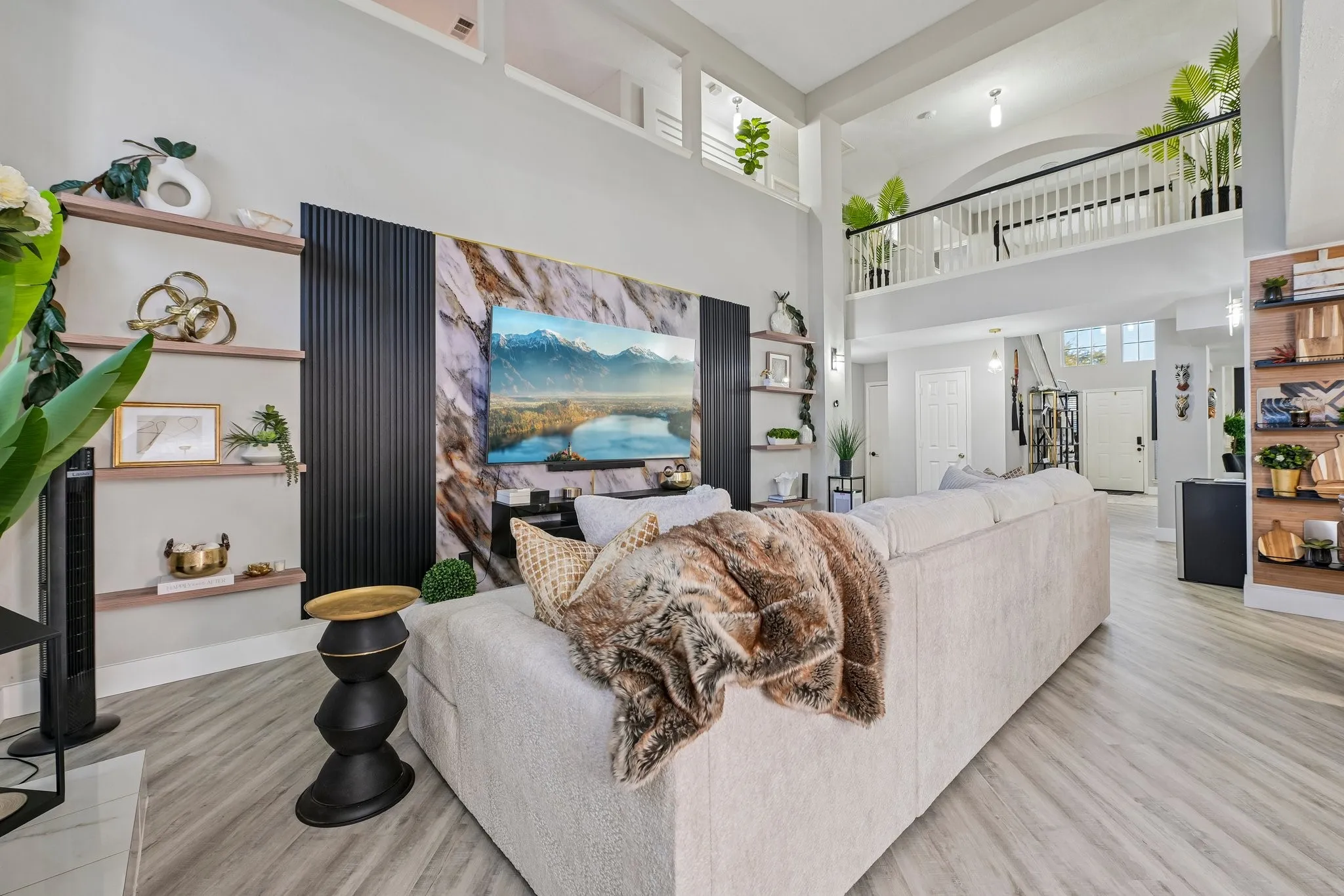 Two-story living area with high ceilings, wood-finish flooring, a decorative accent wall, and built-in shelving