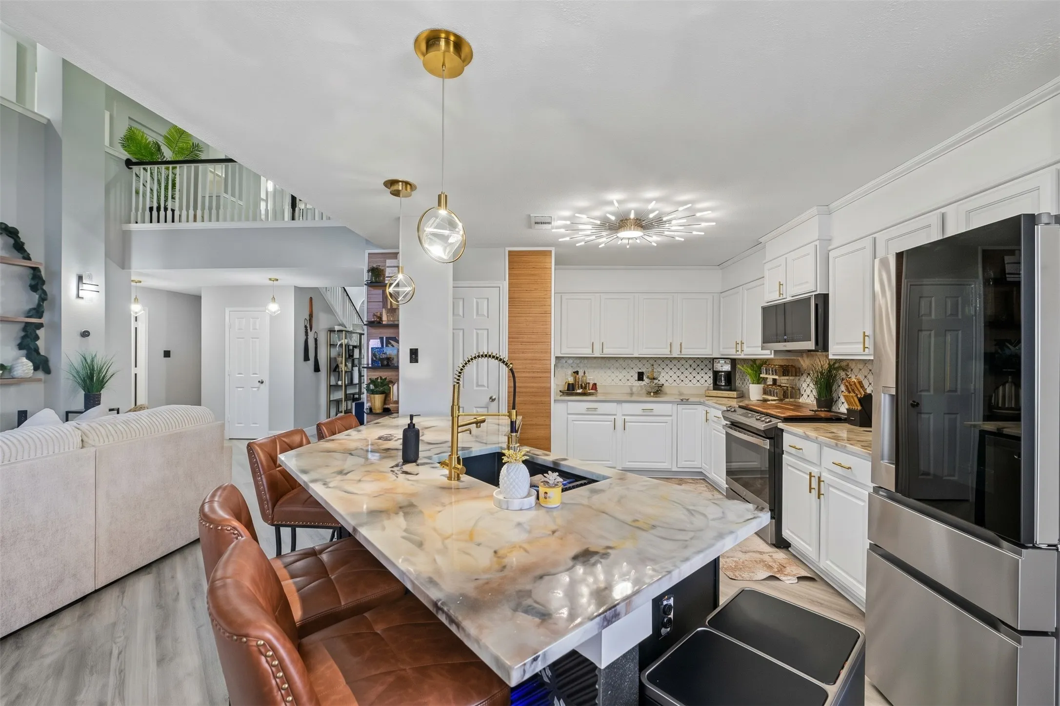 Open-concept kitchen featuring an oversized island, gold-finish fixtures, white cabinetry, and stainless steel appliances