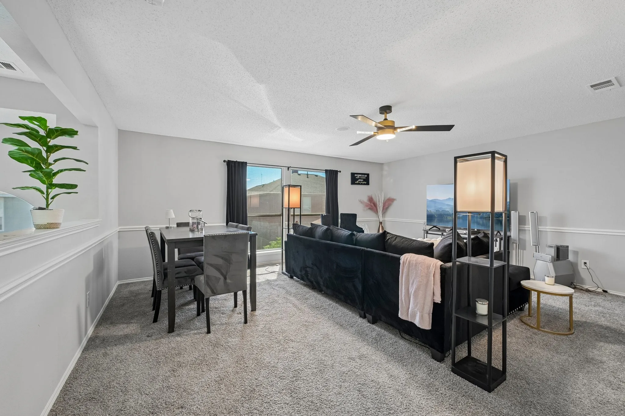 Open-concept living space featuring light gray walls, carpet flooring, a ceiling fan, and sliding glass doors