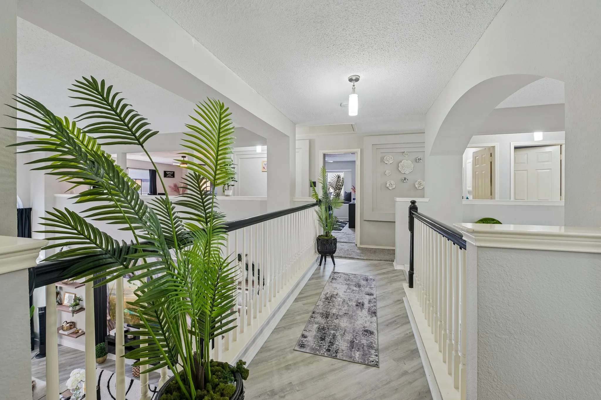 Upper-level hallway with wood-finish flooring, white railing with dark top, and arched architectural detail