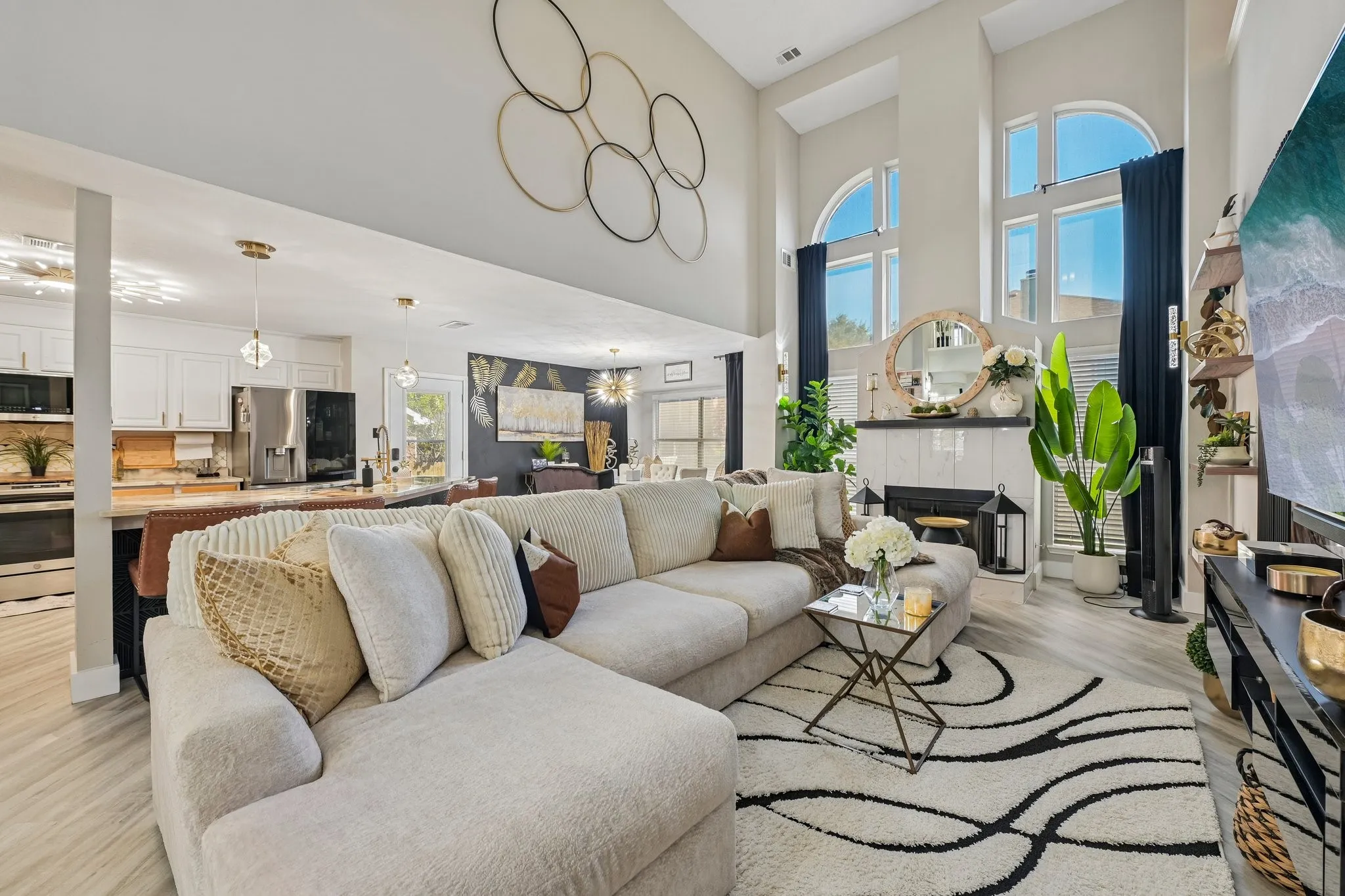 Two-story living area featuring tall arched windows, a fireplace with a white tile surround, and light wood-finish flooring