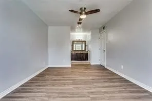 Wood-finish flooring, ceiling fan with integrated lighting, and a white interior door