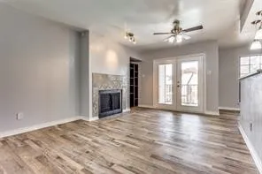 Wood-finish flooring, fireplace with stone tile surround, double French doors, ceiling fan, and recessed lighting