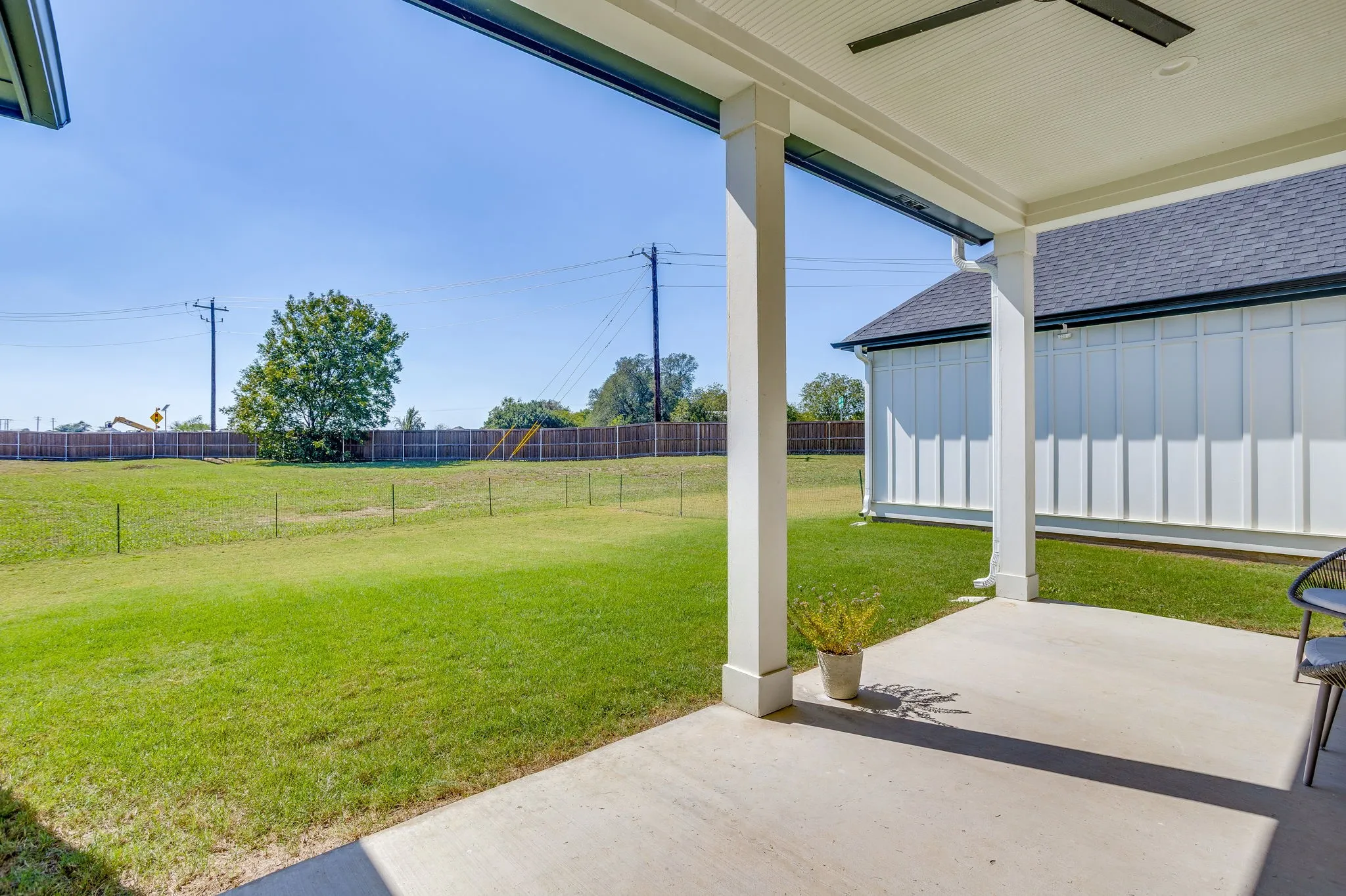 Expansive open-air covered patio with a ceiling fan, concrete flooring, and substantial support columns