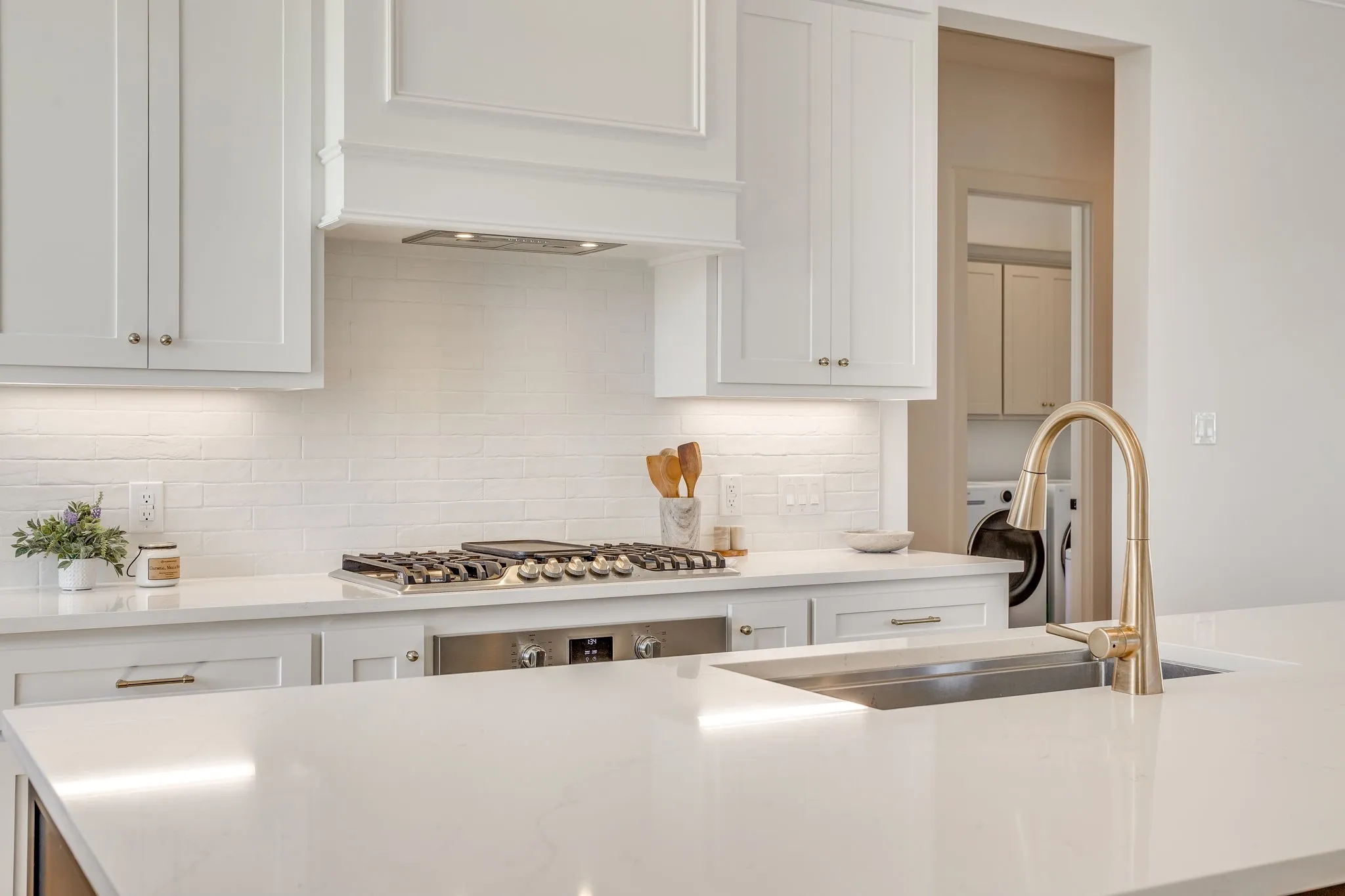 White cabinetry, light-toned countertops, subway tile backsplash, stainless steel gas range, and a gold-finish faucet