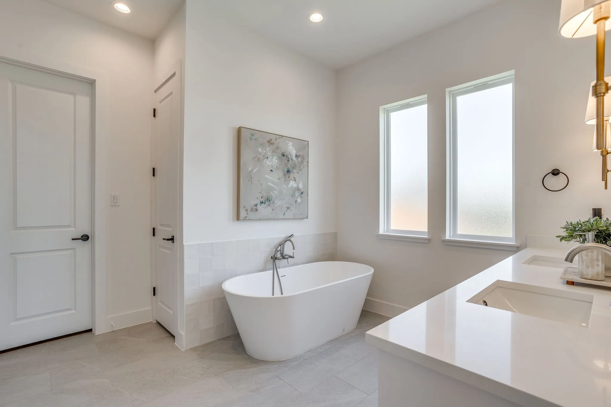 Freestanding soaking tub with floor-mounted faucet, dual vanity with integrated sinks, and two privacy windows