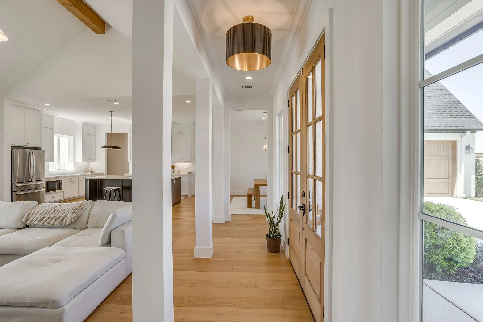 Wood-finish flooring throughout, white painted walls, natural wood entry door with clear glass panels, and a modern ceiling light fixture