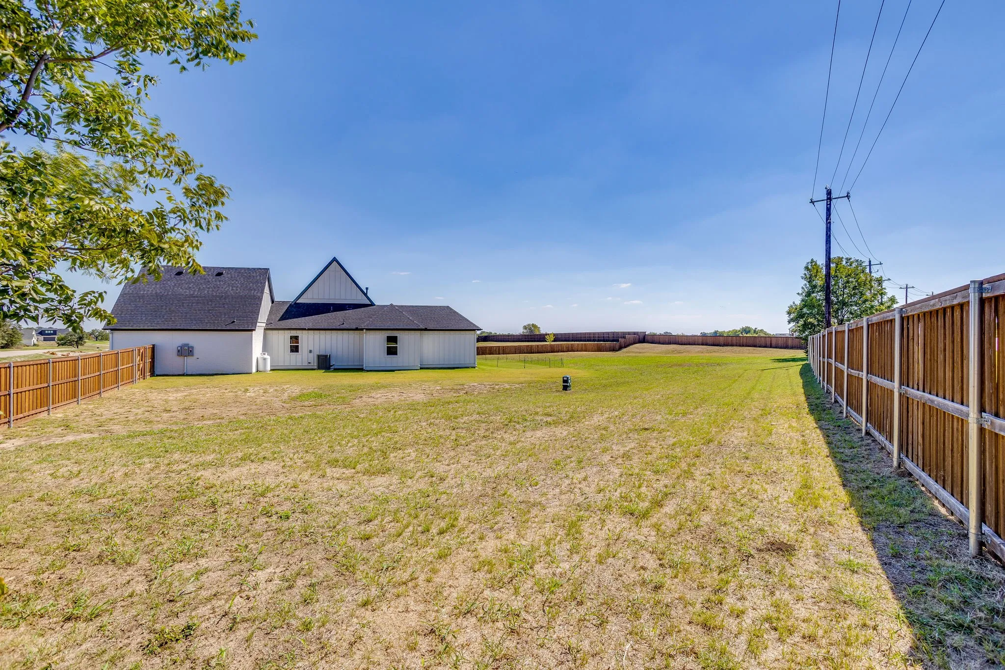 Spacious backyard featuring a wood privacy fence, expansive grassy area, and a white exterior residence with a dark shingle roof