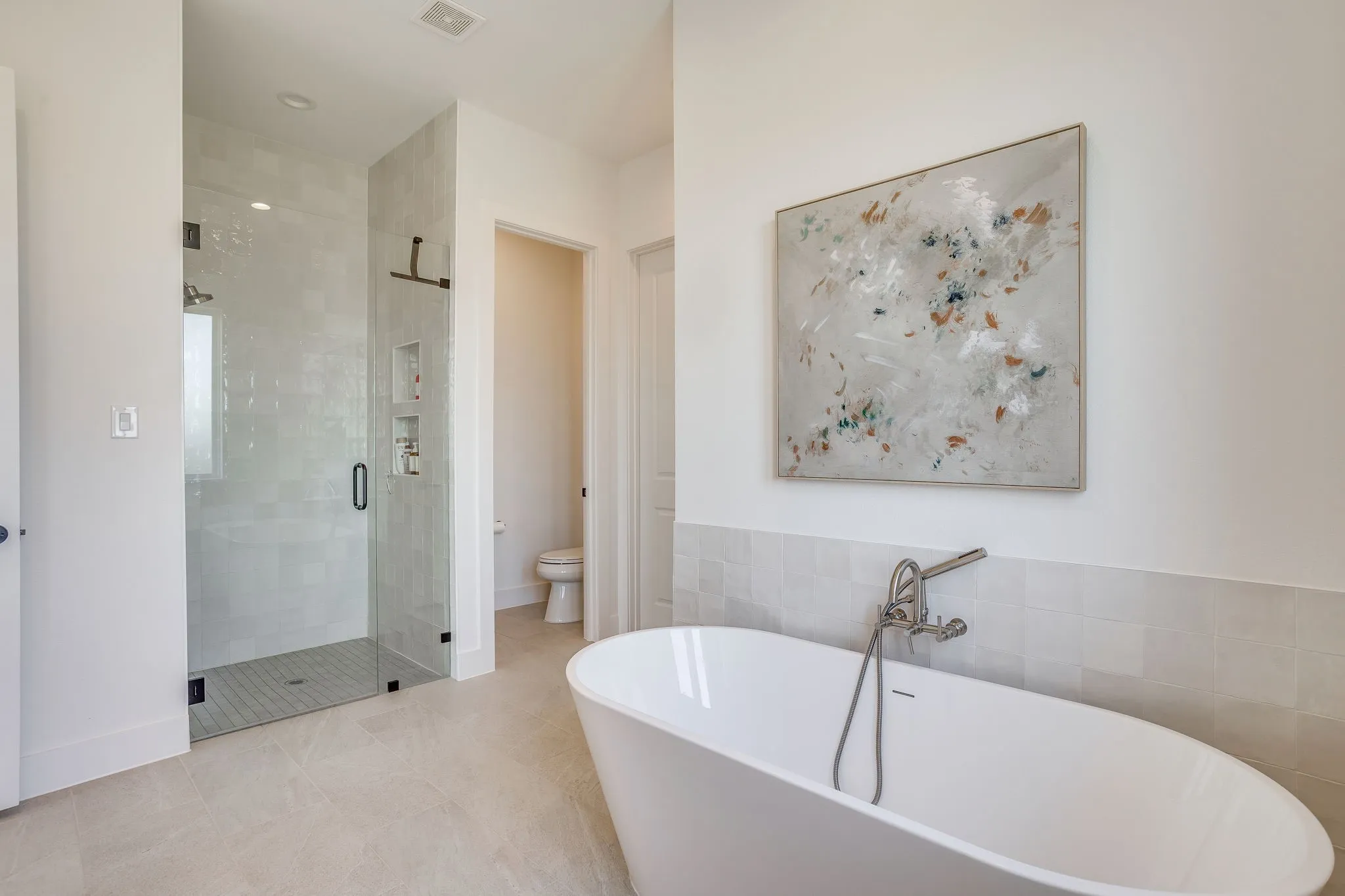 Freestanding soaking tub with brushed nickel fixtures, glass-enclosed shower with subway tile surround, recessed shower niches, and light tile flooring