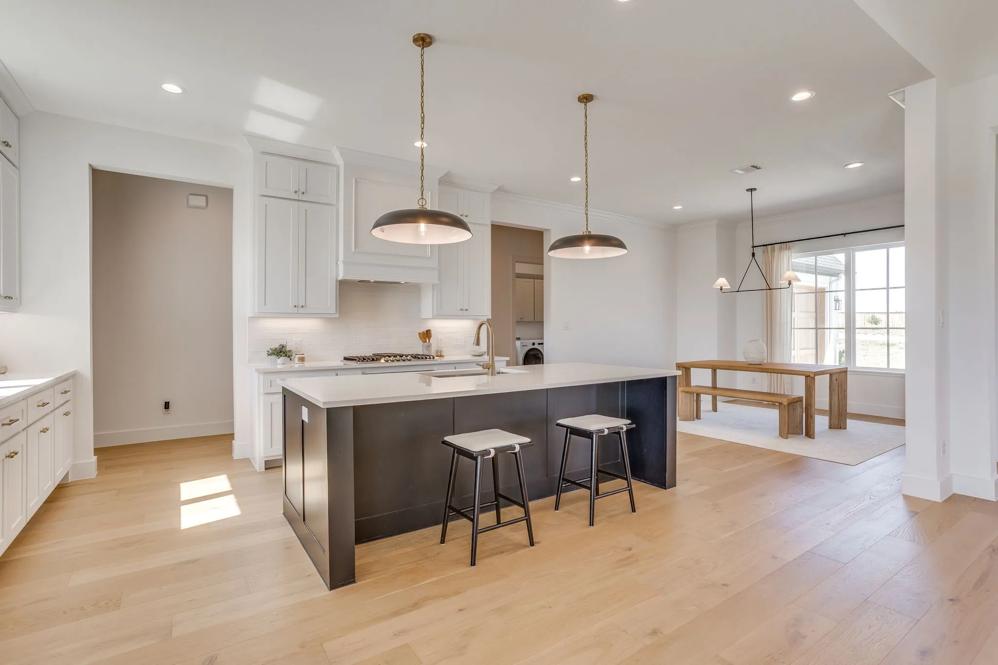 Open-concept kitchen featuring a dark-toned island with counter seating, light wood-finish flooring, white cabinetry, and recessed lighting