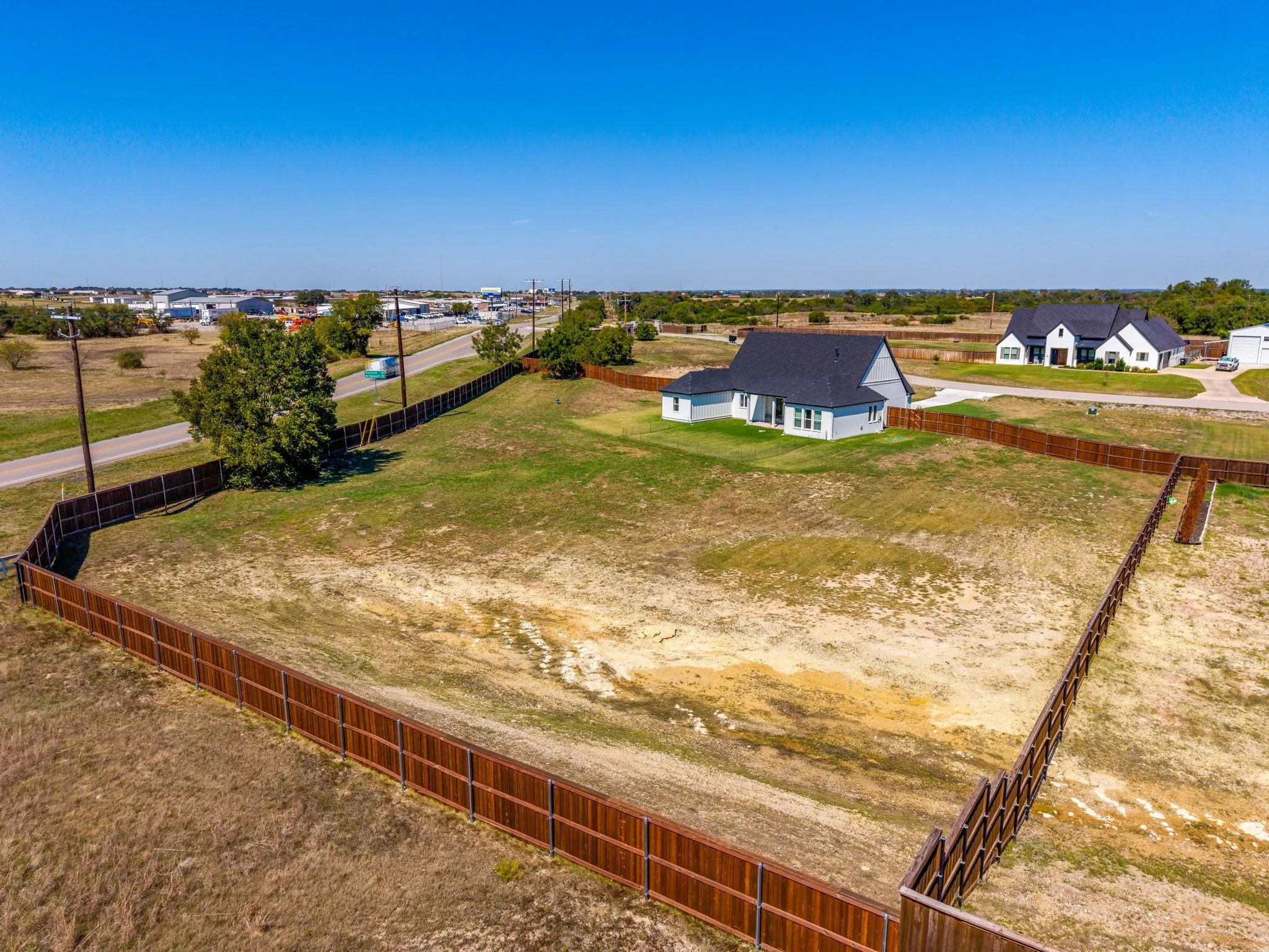 Expansive lot with full perimeter wood fencing and a newly constructed residence featuring light-colored siding and a dark roof