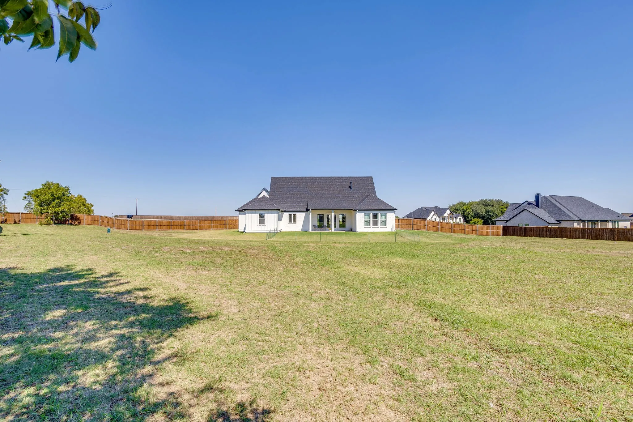 Expansive backyard featuring a manicured lawn, full wood fencing, and a white exterior with a dark roof