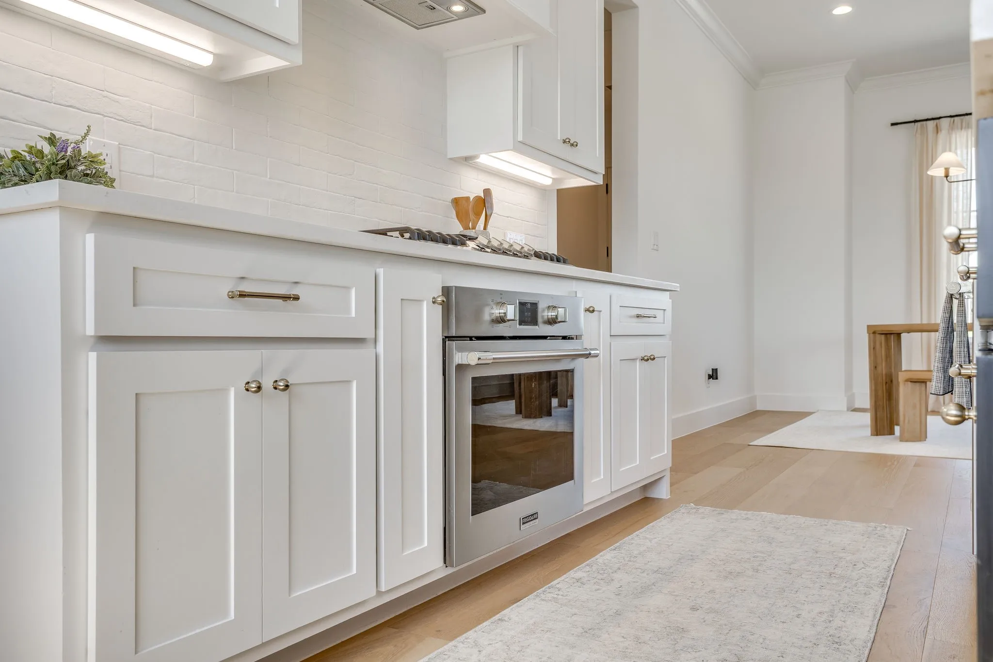 White shaker cabinetry with modern hardware, stainless steel built-in oven, light-toned wood-finish flooring, and crown molding