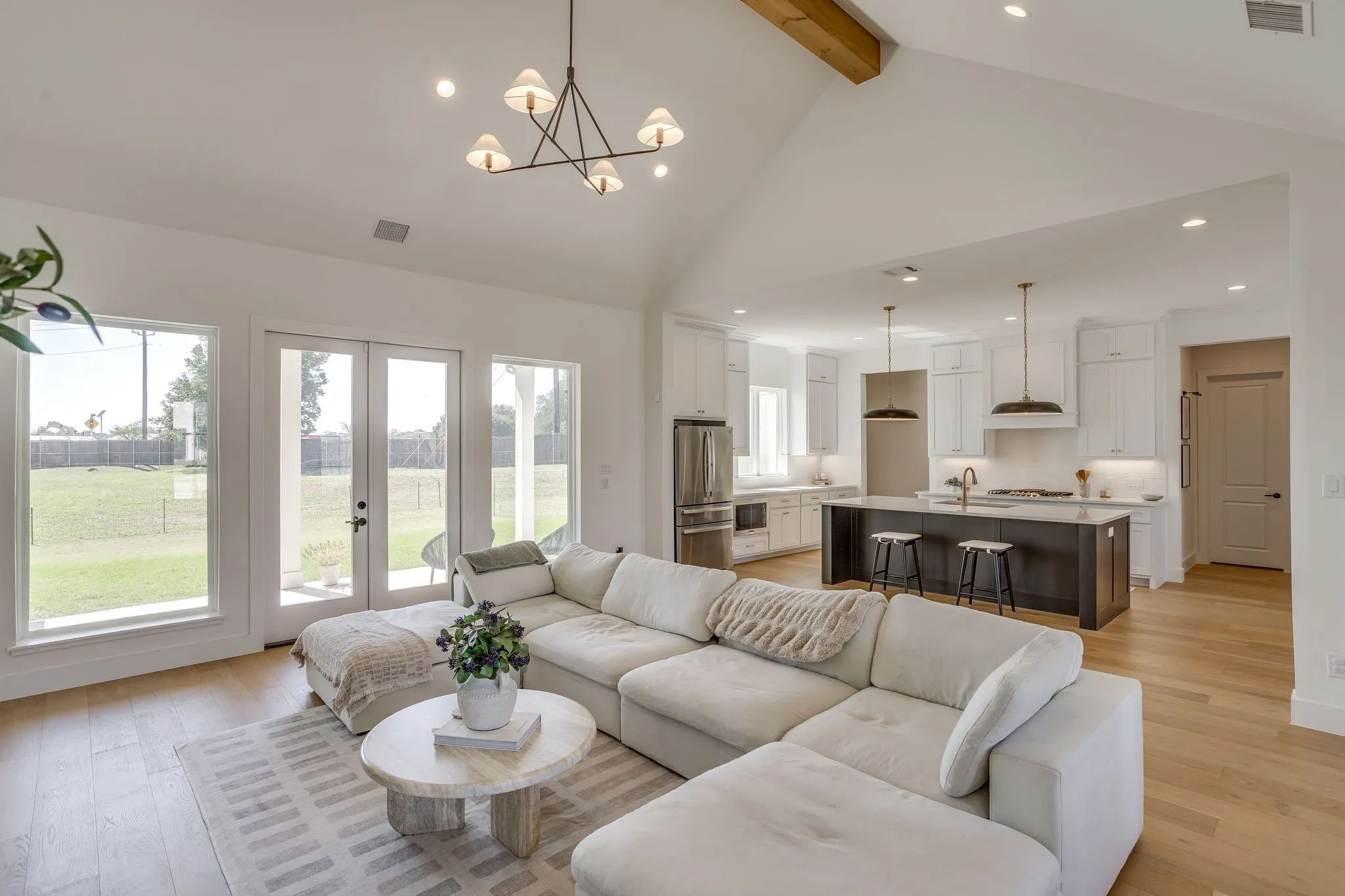 Vaulted ceiling with exposed wood beam, wood-finish flooring, recessed lighting, and a modern chandelier