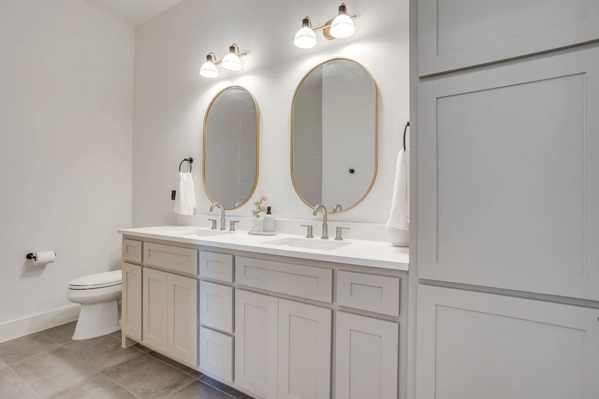Dual vanity with individual oval mirrors and overhead lighting
