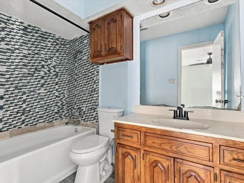 Tub and shower combination with mosaic tile surround, wood-finish vanity with integrated sink, and wall-mounted wood-finish cabinet