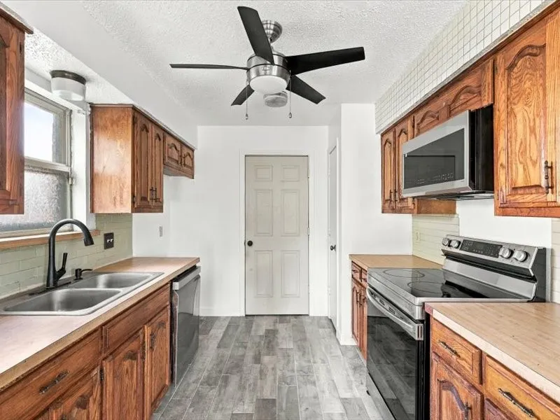 Kitchen featuring wood-finish cabinetry, stainless steel appliances, a double basin sink with a matte black faucet, wood-finish countertops, and wood-finish flooring