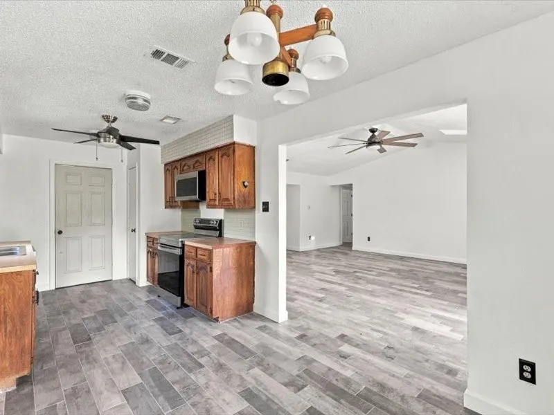 Kitchen featuring wood cabinetry, stainless steel microwave, and wood-finish flooring extending into an adjacent living area with a ceiling fan