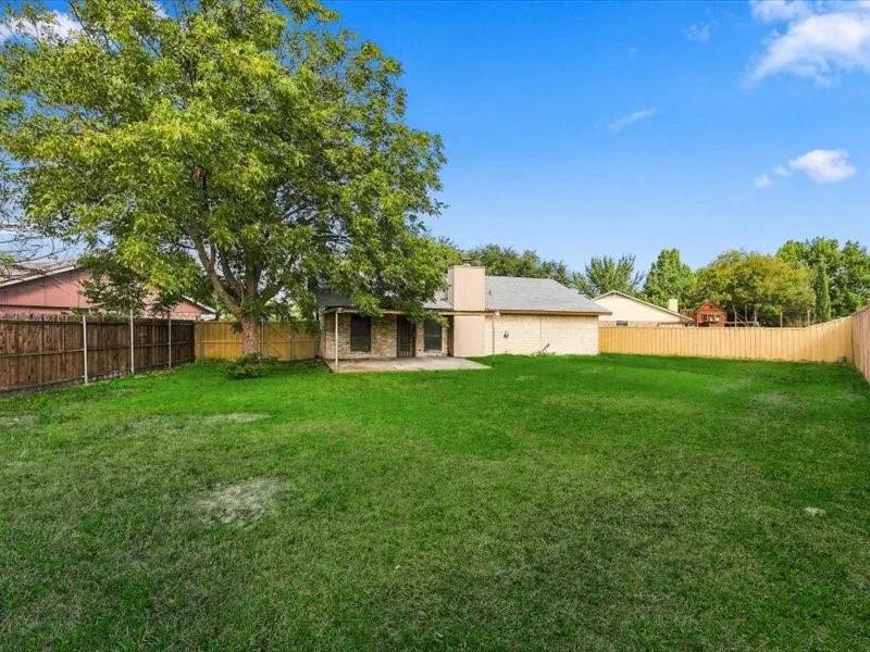 Expansive grassy backyard featuring a paved patio and mature trees