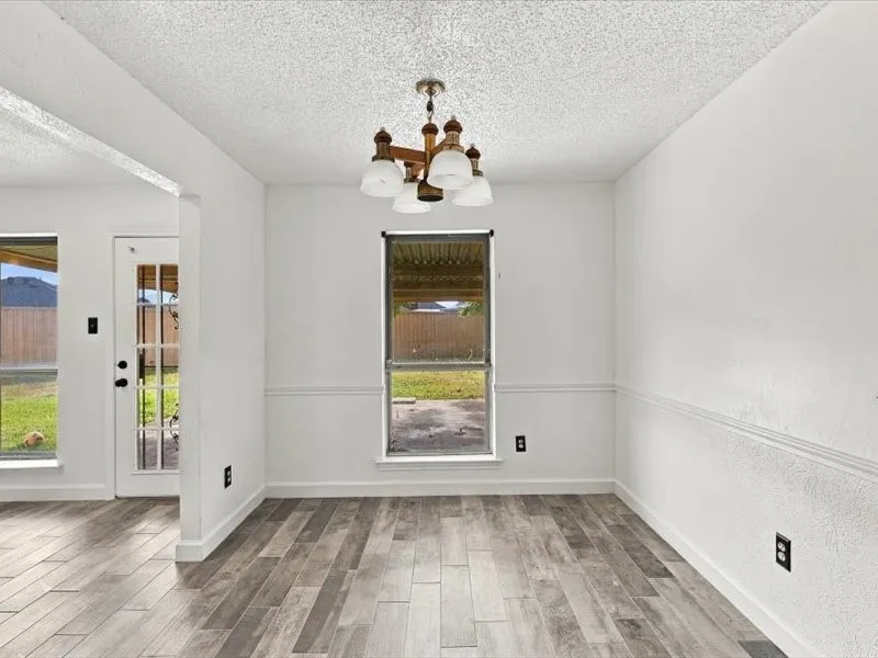Wood-finish flooring with a decorative chandelier, white painted walls with chair rail molding, and multiple windows