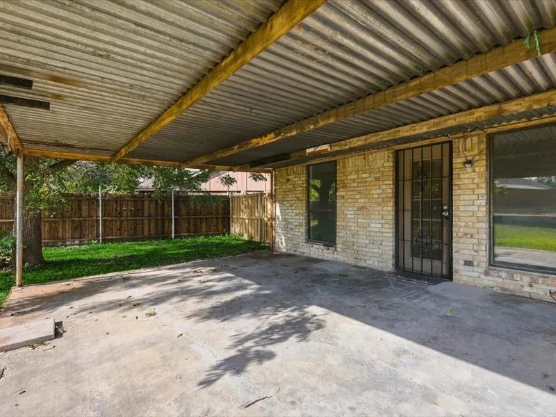 Covered patio area with a concrete surface, a corrugated metal roof, and a brick exterior wall