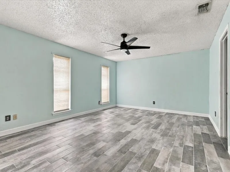Wood-finish tile flooring, a ceiling fan, and two windows with blinds