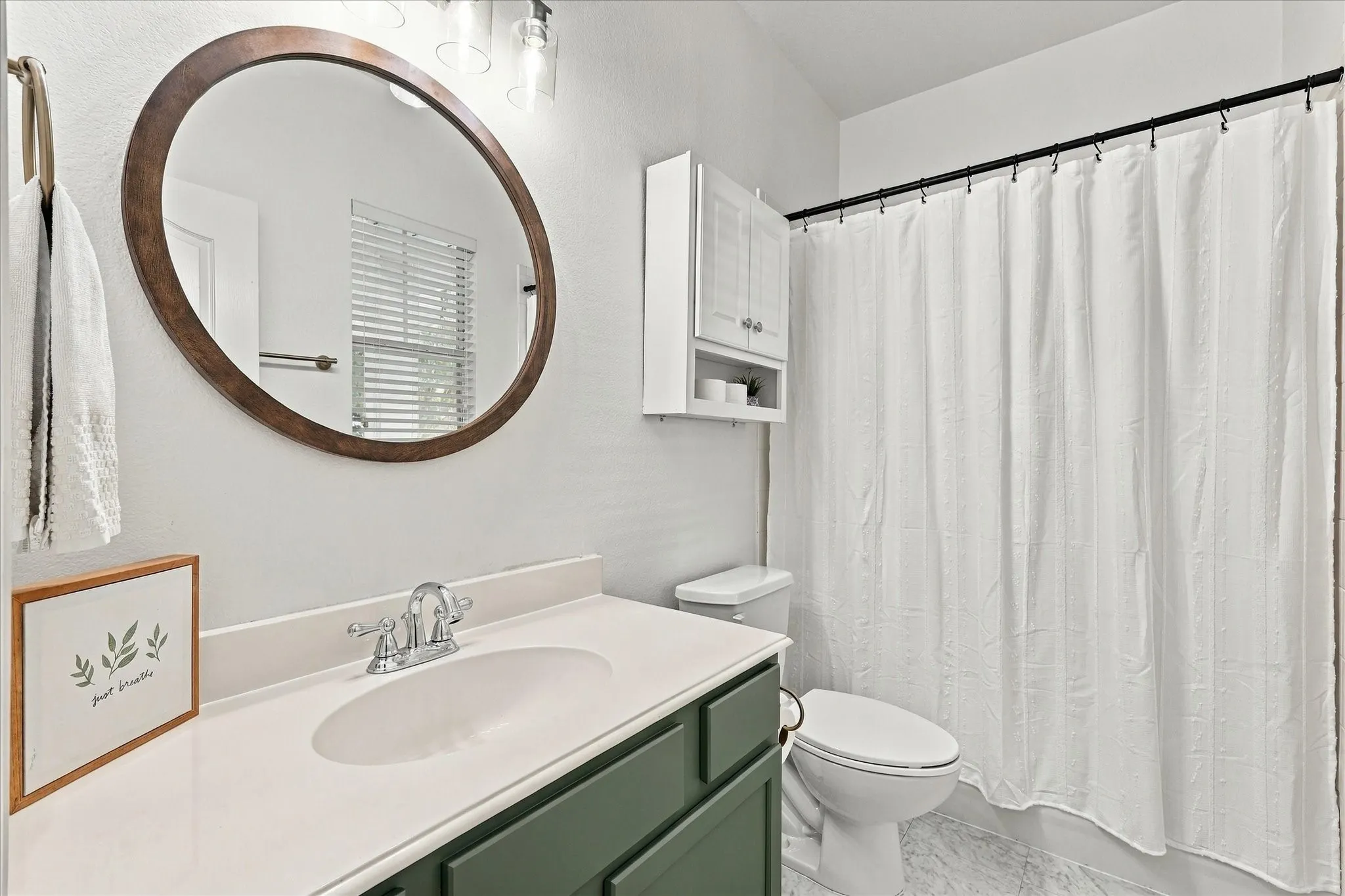 Bathroom featuring a vanity with a white countertop, oval wood-updated framed mirror, updated lighting and built-in wall cabinets!