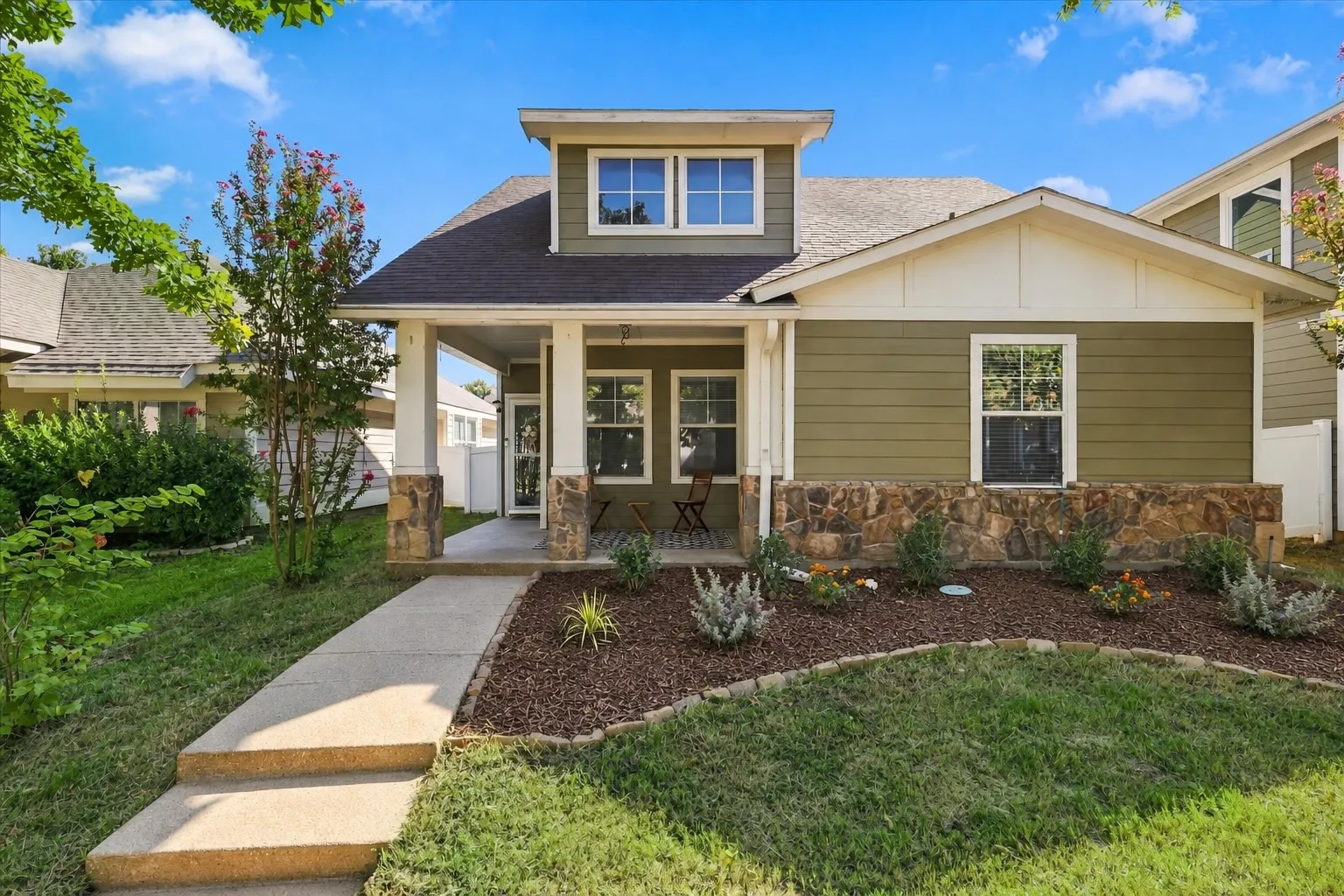 Welcoming covered front porch with stone-wrapped columns, complemented by a stone facade