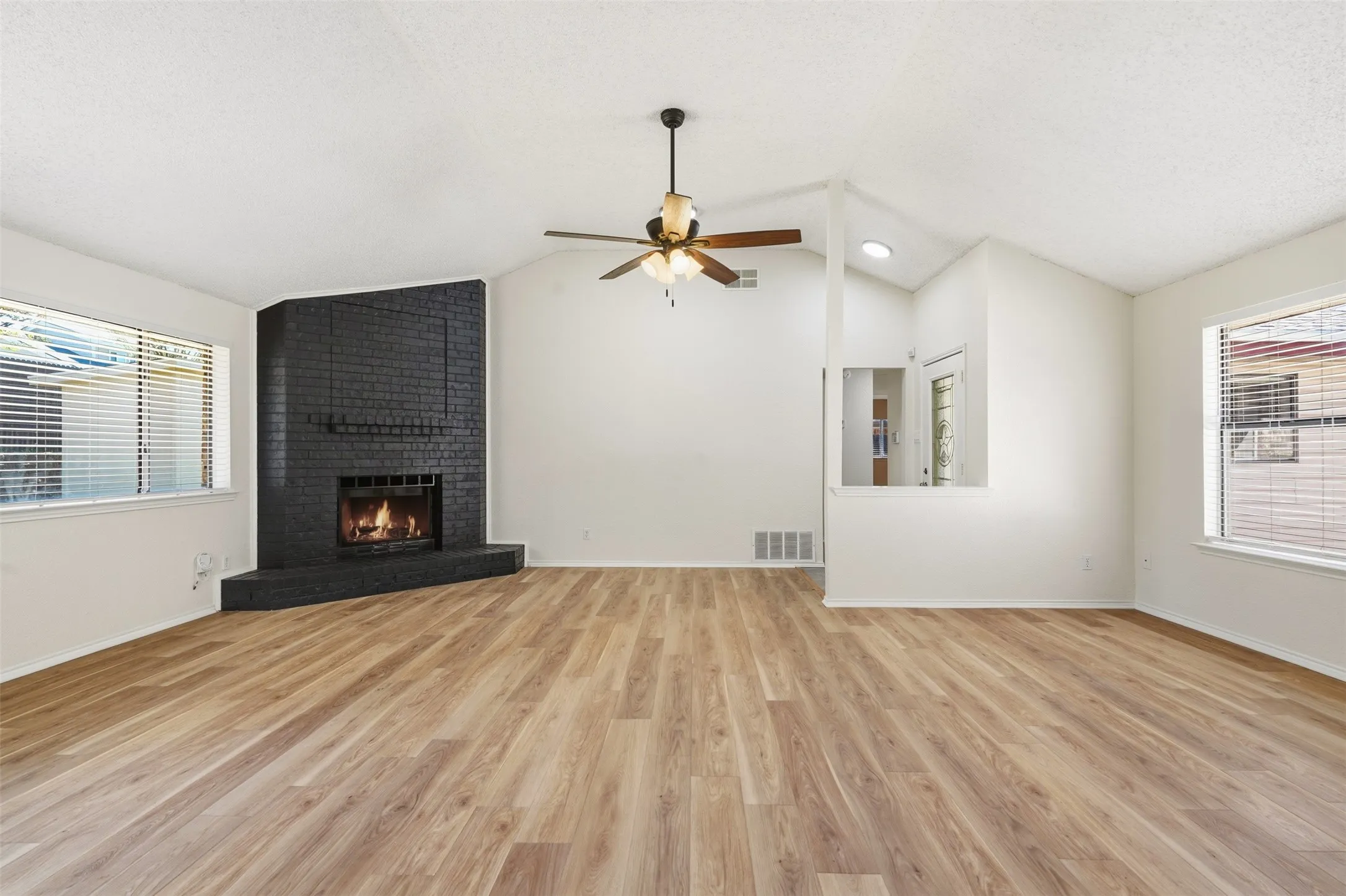 Vaulted ceiling, wood-finish flooring, corner brick fireplace, ceiling fan, and multiple windows