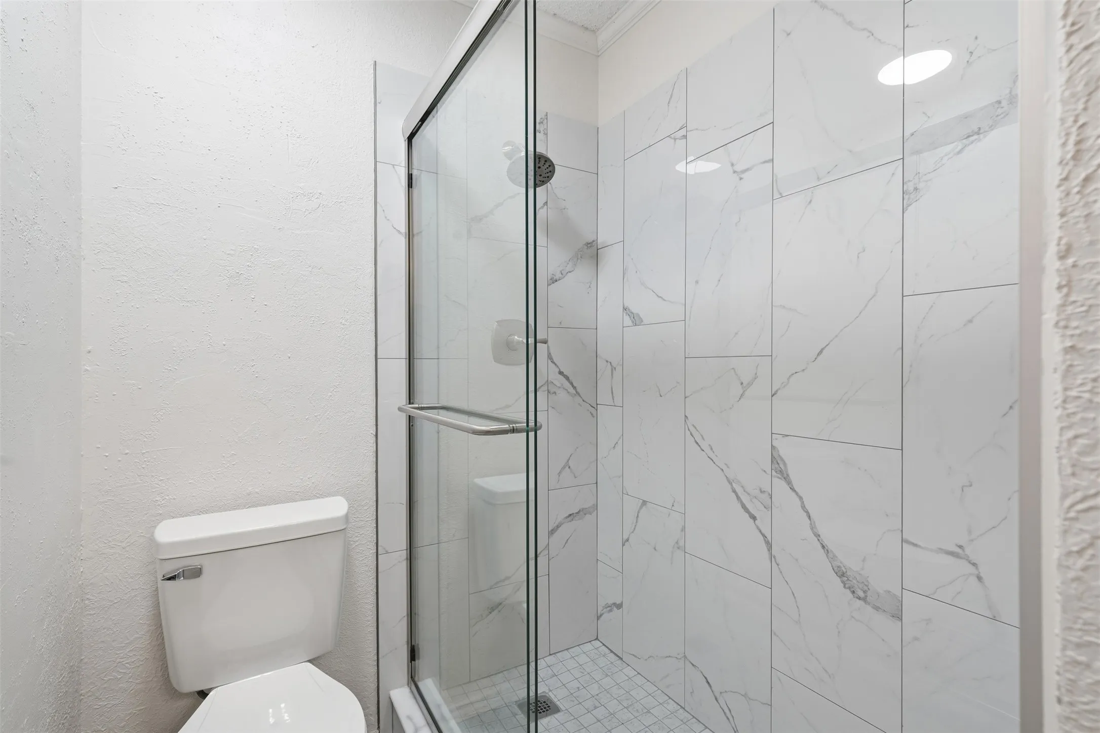 Frameless glass shower enclosure with a chrome handle, white subway tile shower walls with grey veining, and a tiled shower floor