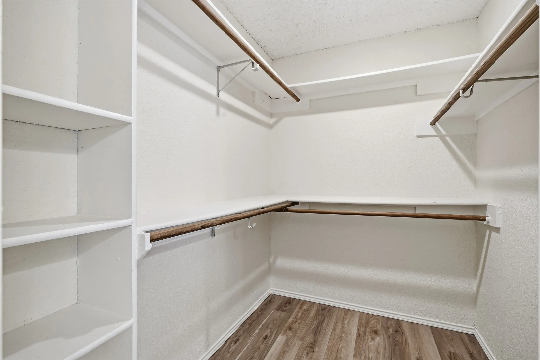 Walk-in closet featuring built-in shelving, multiple hanging rods, and wood-finish flooring