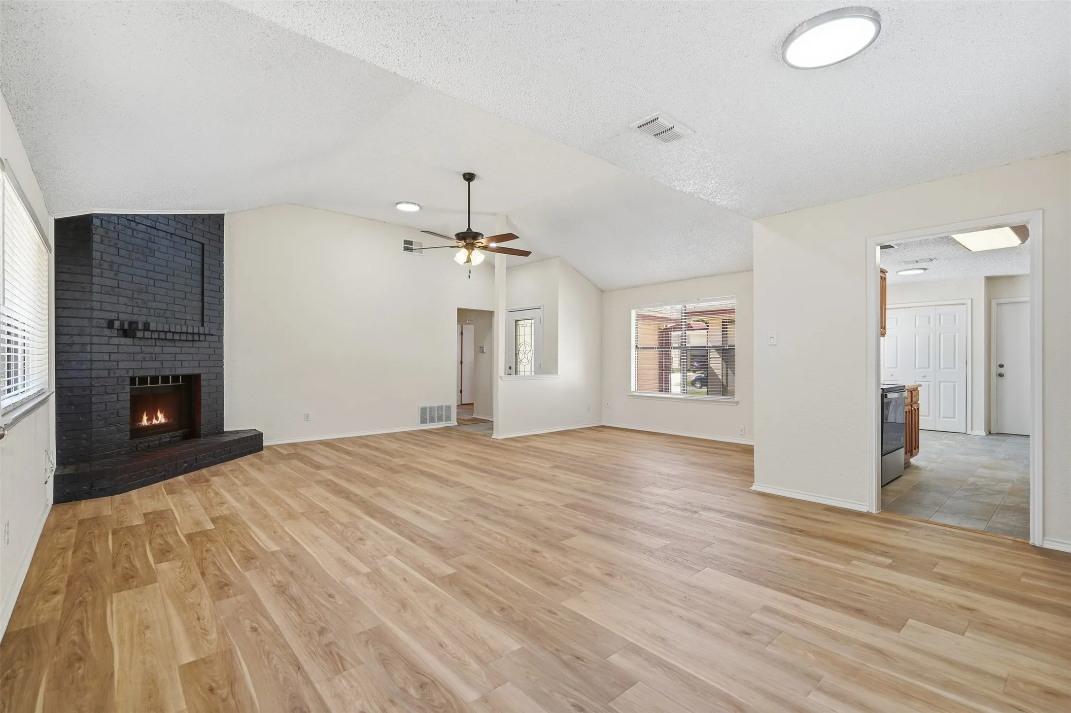 Spacious living area featuring a black brick fireplace, wood-finish flooring, vaulted ceiling, and recessed lighting